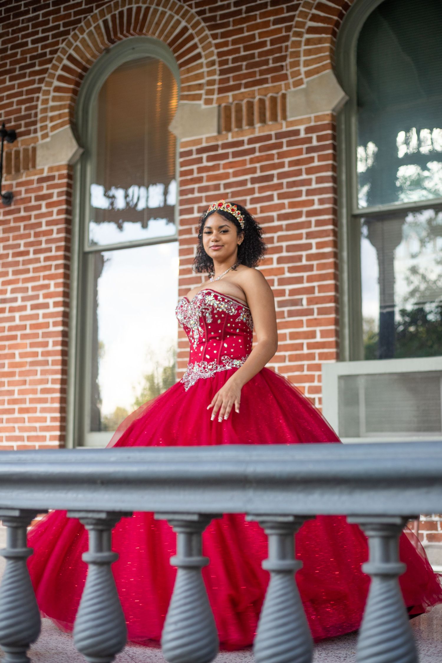 Red formal dress session on historic brick building porch with grey railings.