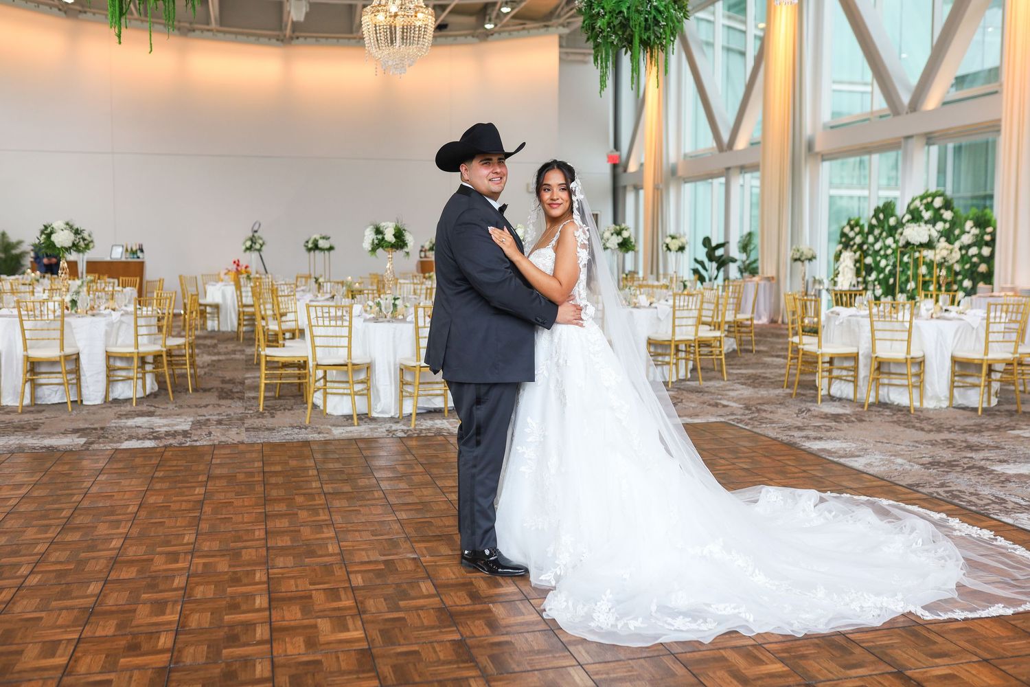 Bride and groom dancing in elegant wedding reception hall with gold chairs and floral arrangements.