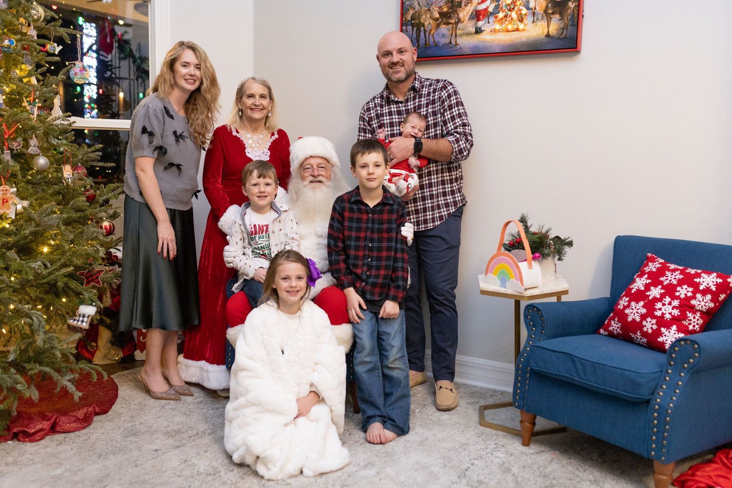 A living room decorated for Christmas with a blue sofa and holiday artwork on the wall.