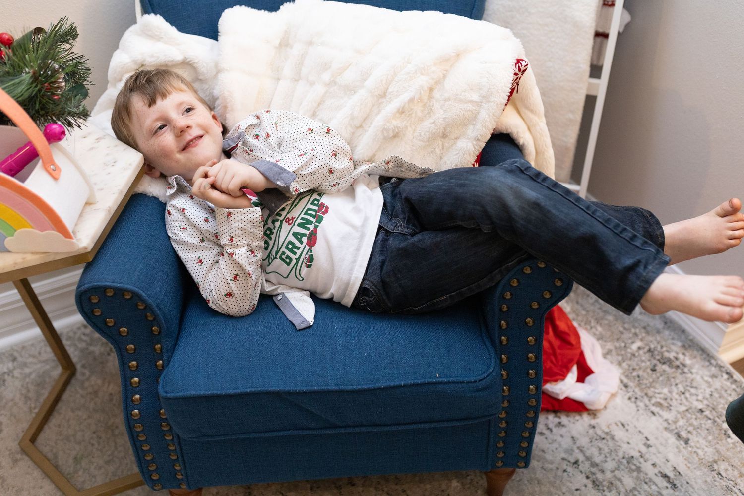 A young person lounges casually on a blue velvet sofa with decorative studs.