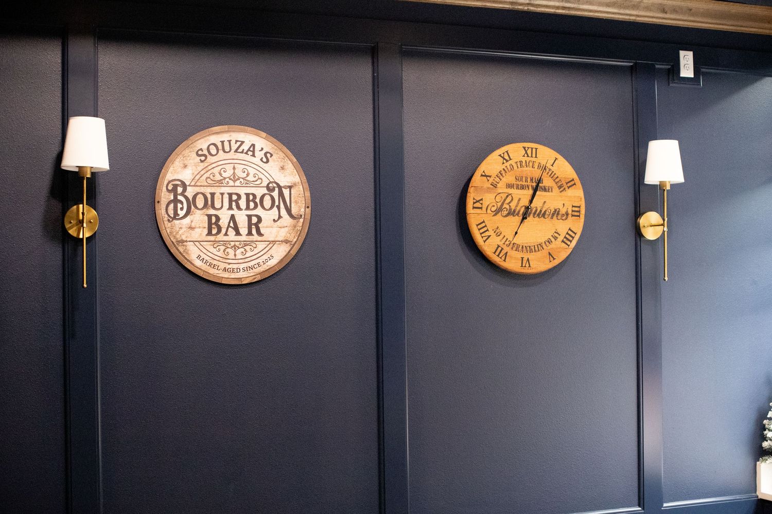 Bar interior with bourbon-themed wooden barrel signs mounted on dark gray walls.