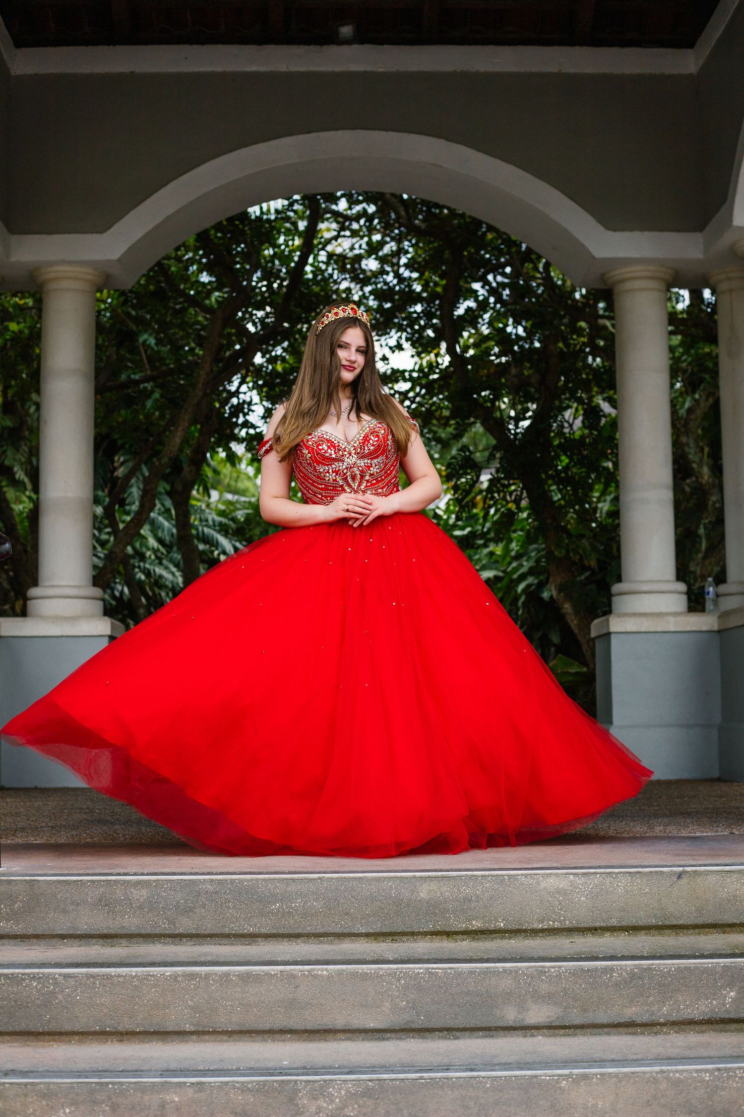 A dramatic red ball gown with beaded bodice photographed under a white columned gazebo.