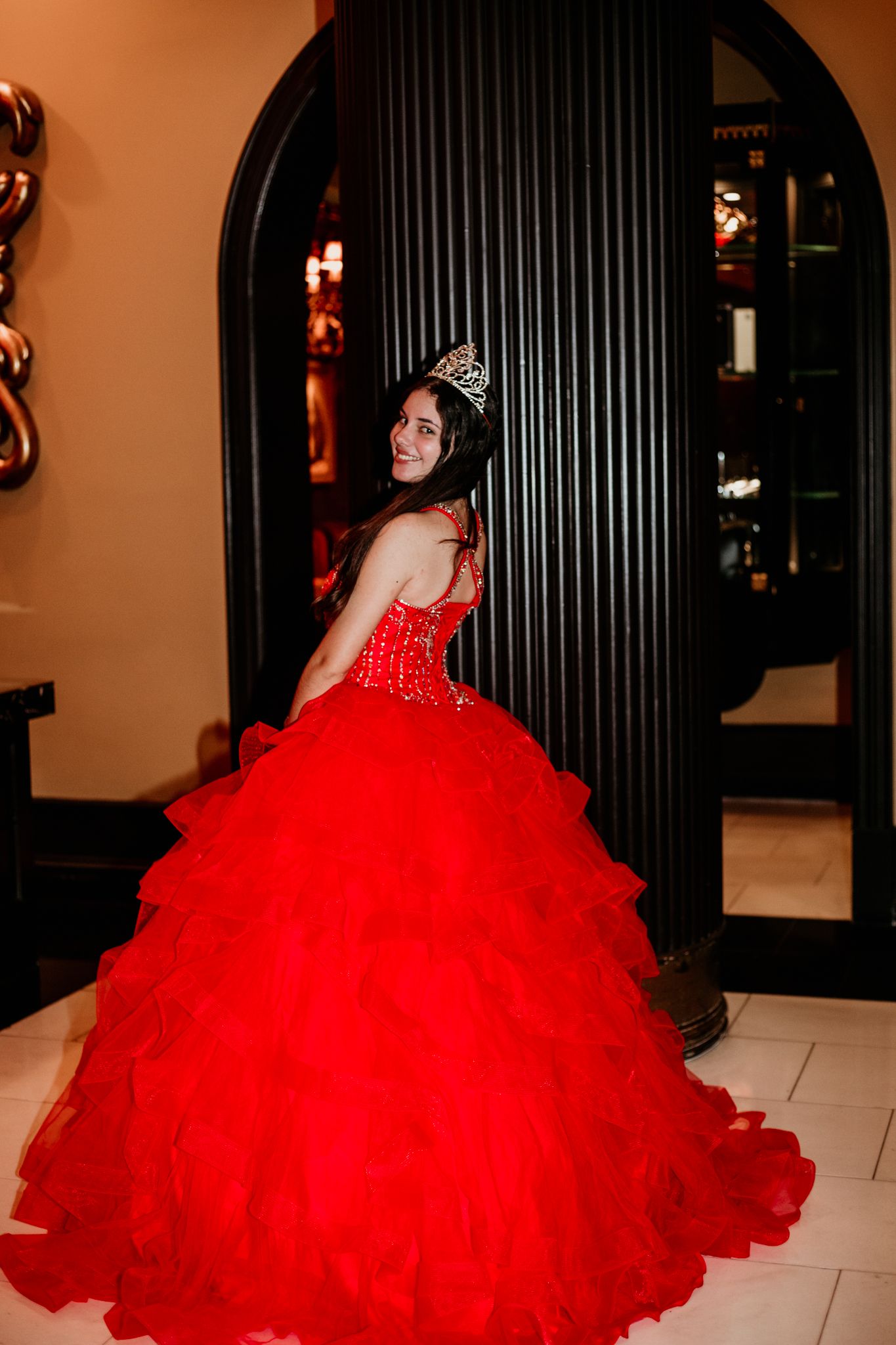 A dramatic red ballgown with ruffled tulle skirt photographed against dark archways.