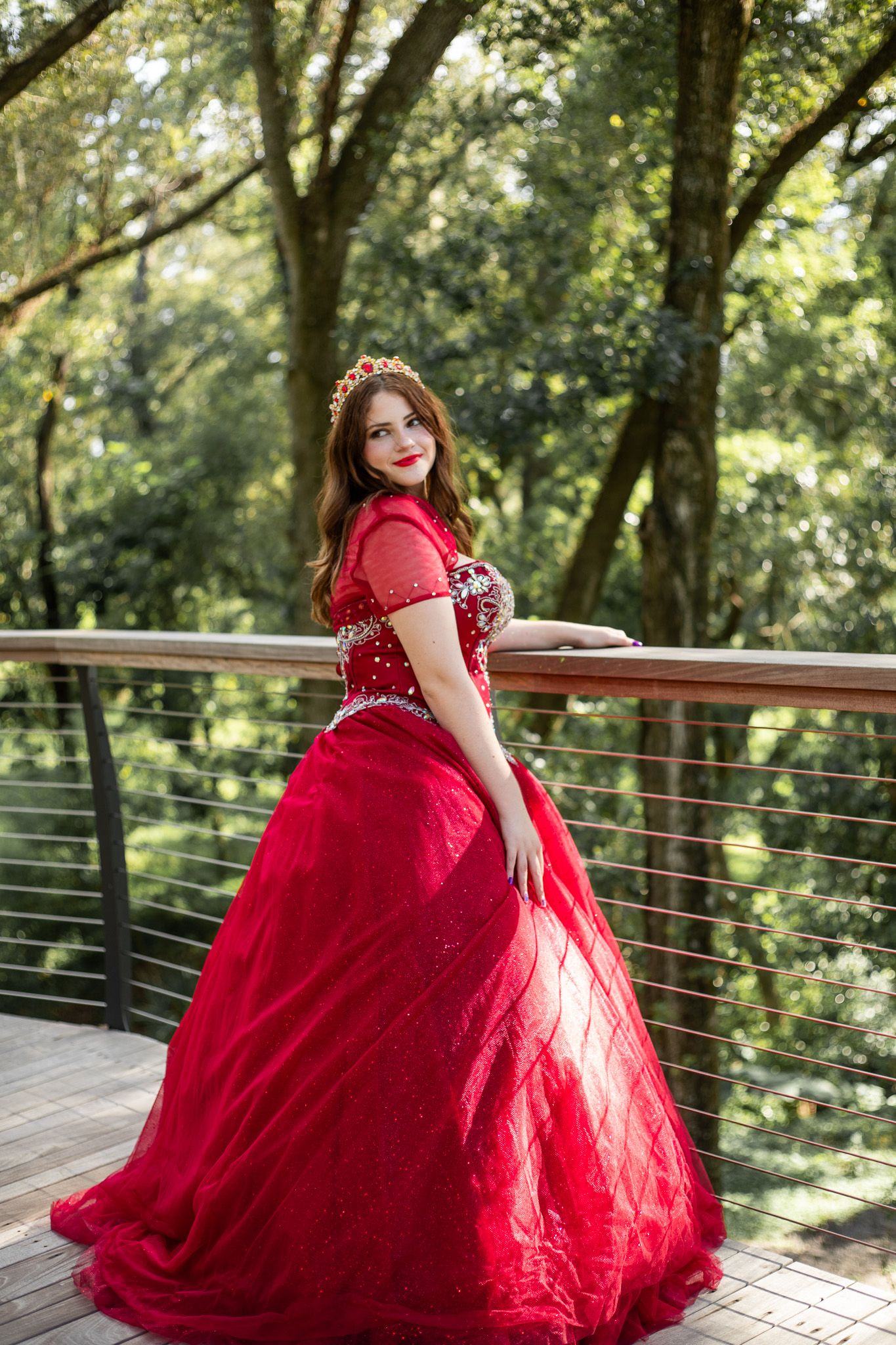 Flowing red ball gown with cap sleeves captured in an outdoor photoshoot on a wooden deck.