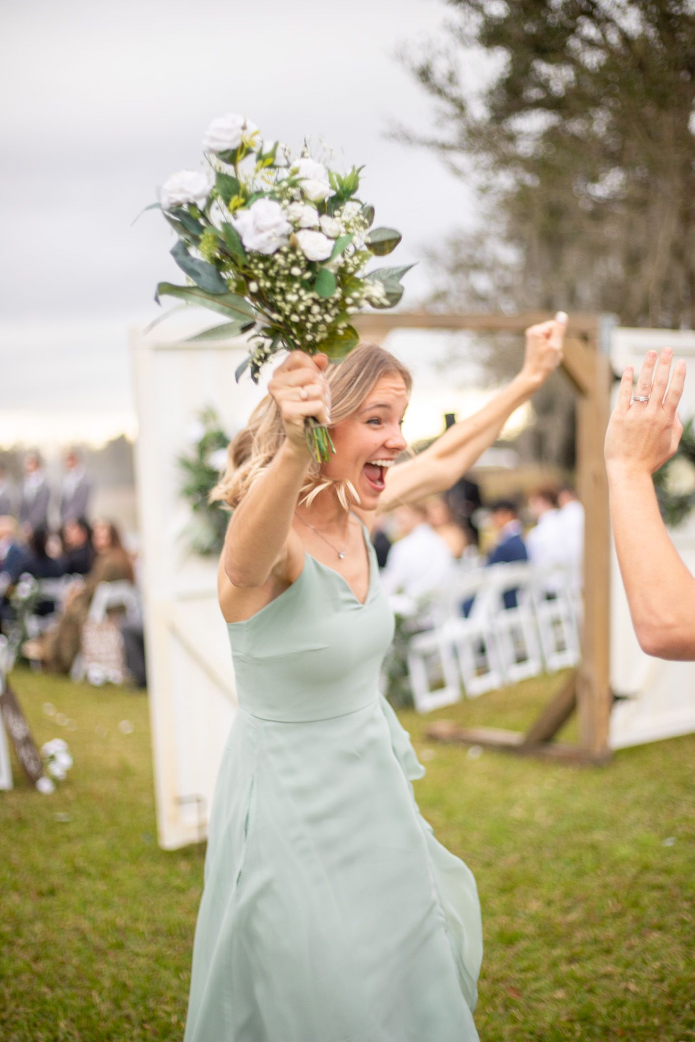 Bridesmaid in mint green dress celebrates joyfully during outdoor ceremony.