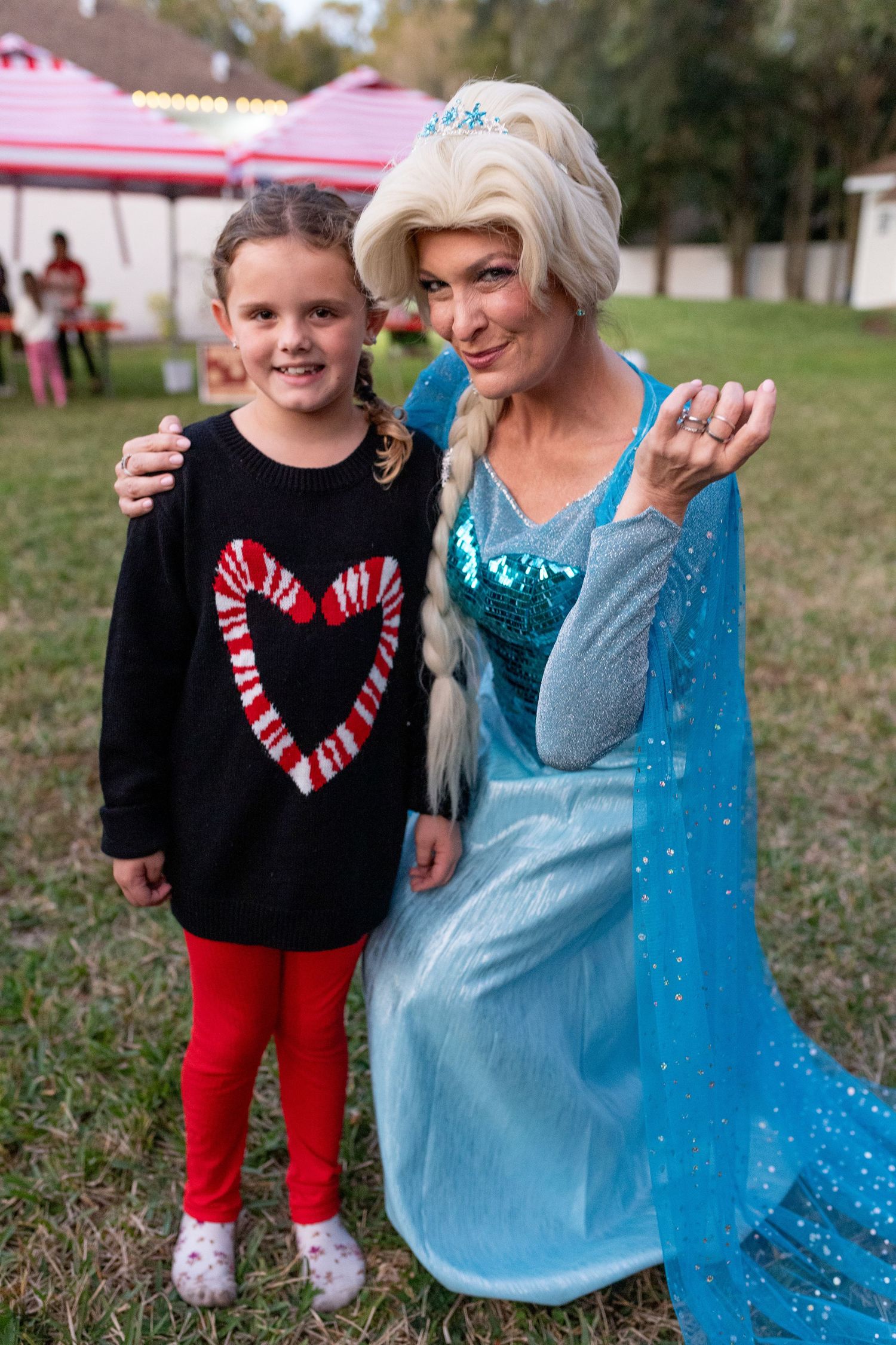 A festive outdoor scene with someone wearing a sparkly blue dress posing with a child in red pants.