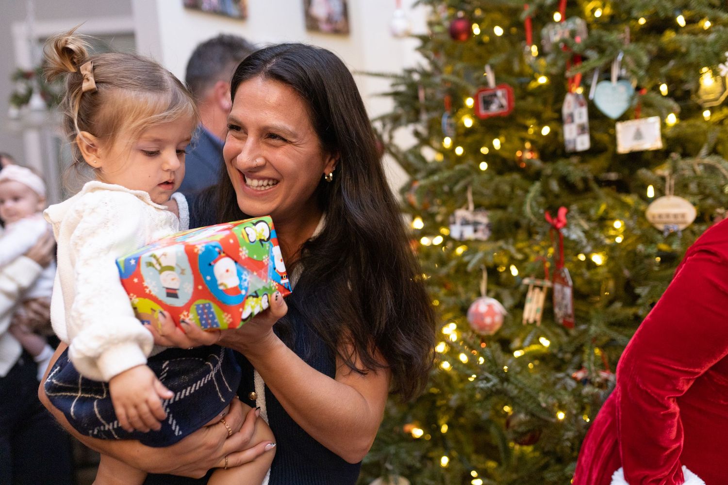 Parent and child share excitement over a Christmas gift by a decorated tree.