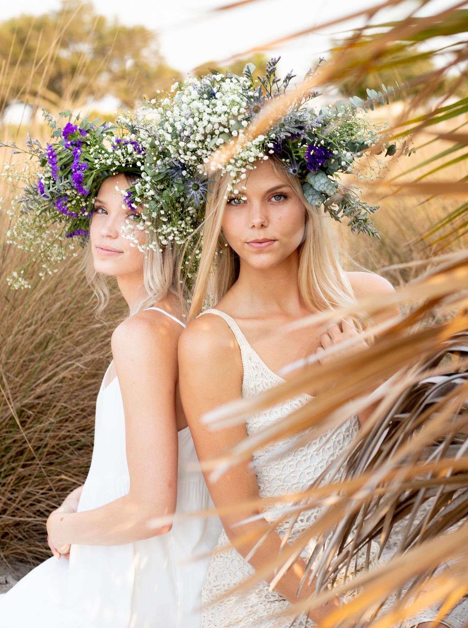 Ethereal portrait of two women in white with floral crowns among beach grass.