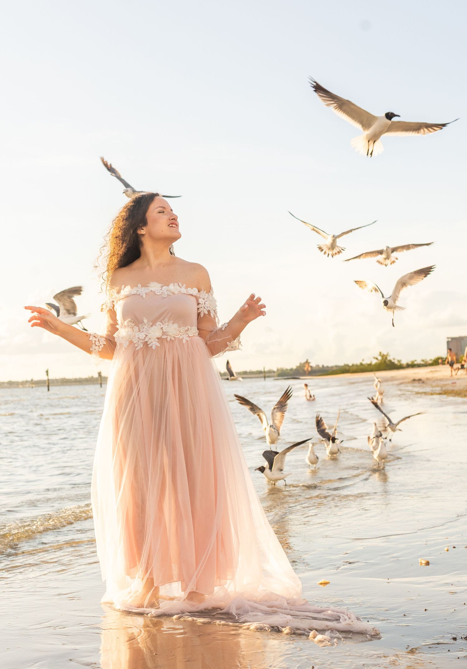 Dreamy beach photography with seagulls flying around a flowing peach-colored dress.