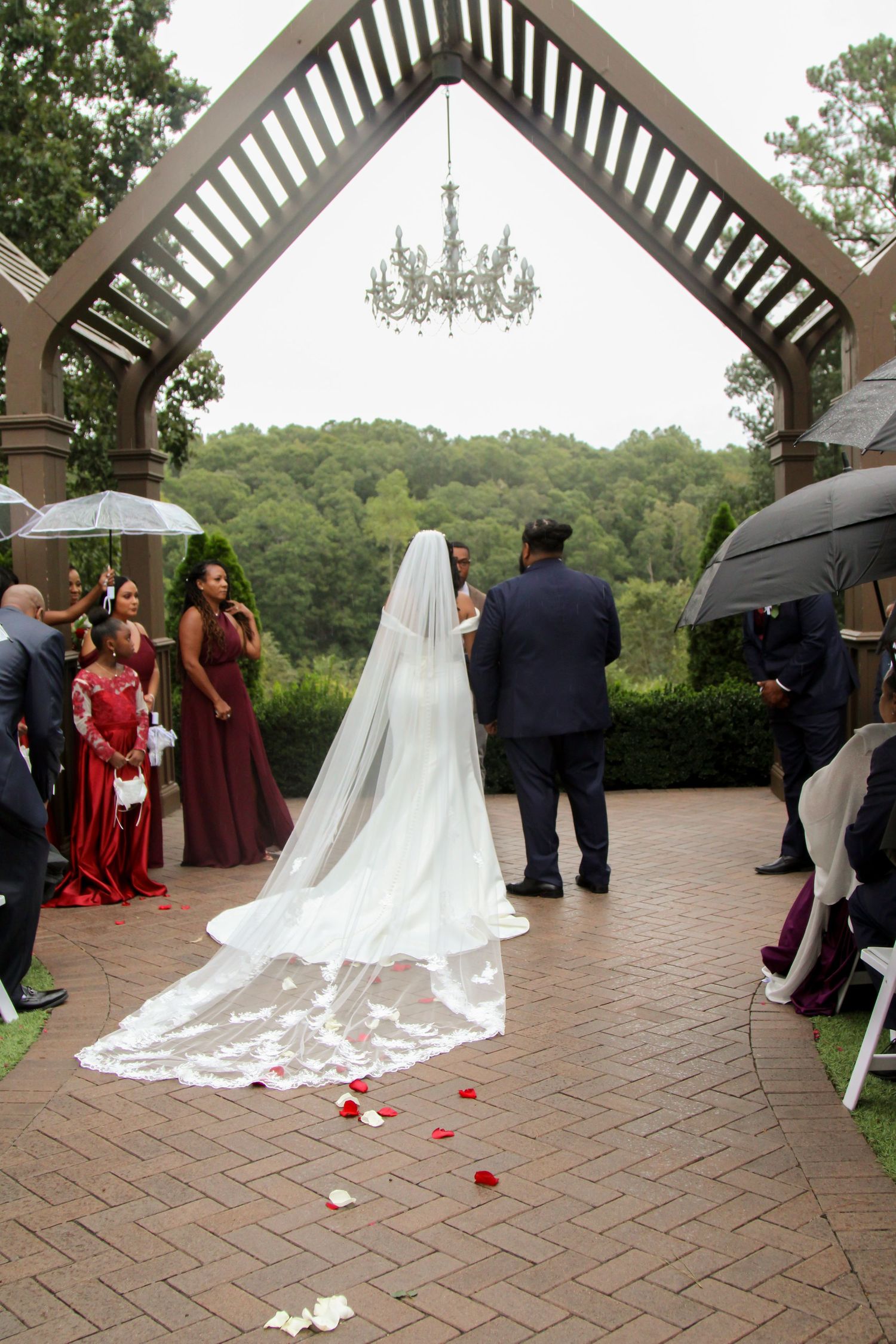 Wedding ceremony procession under white gazebo with scattered rose petals on brick patio.