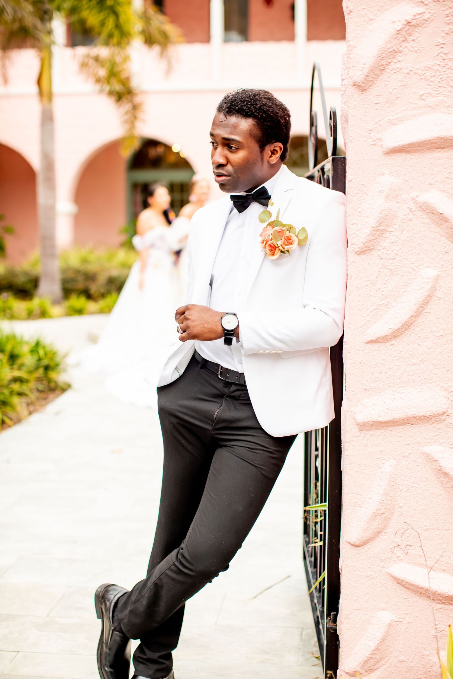 Stylish portraits showcasing formal wear against a textured coral-colored wall with landscaping.