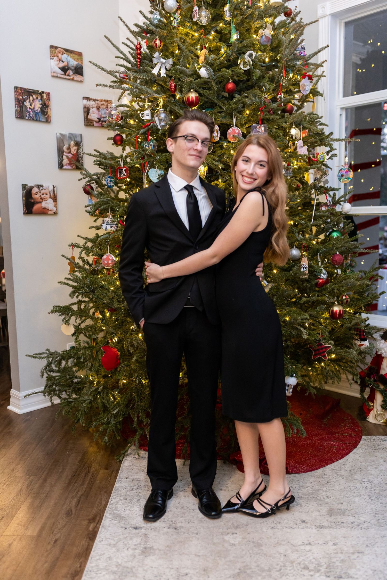 Formal couple poses in front of a Christmas tree for holiday photos.