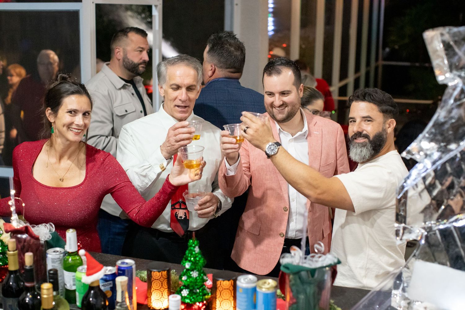 Friends gathered around a bar counter with various bottles raising drinks together.
