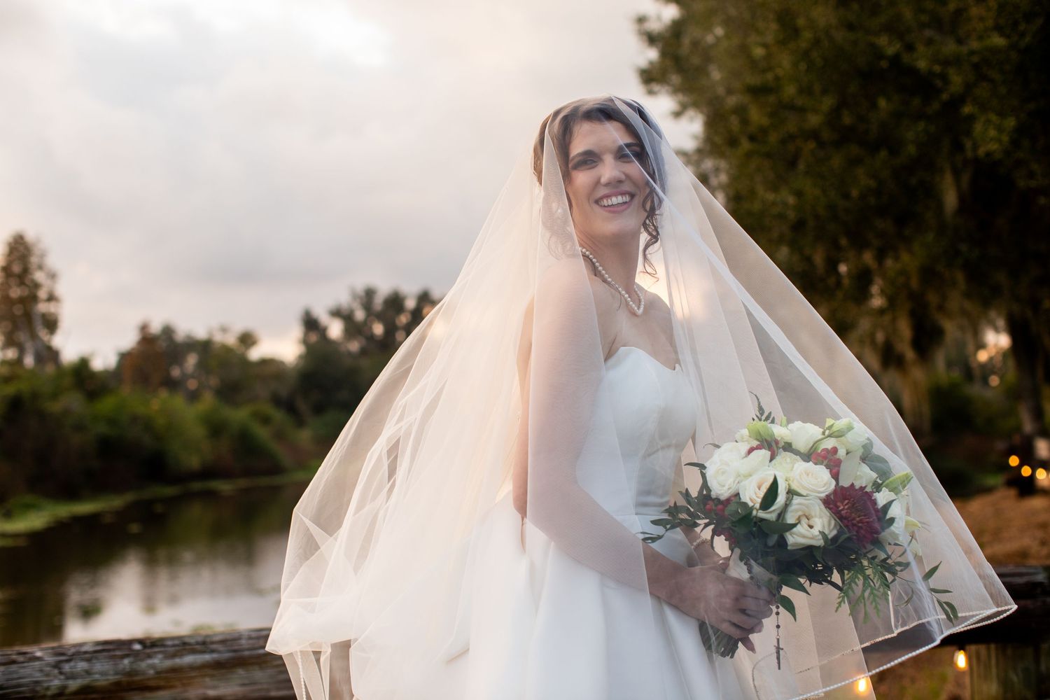 A romantic sunset wedding photo showing a couple embracing while holding a bouquet of flowers.