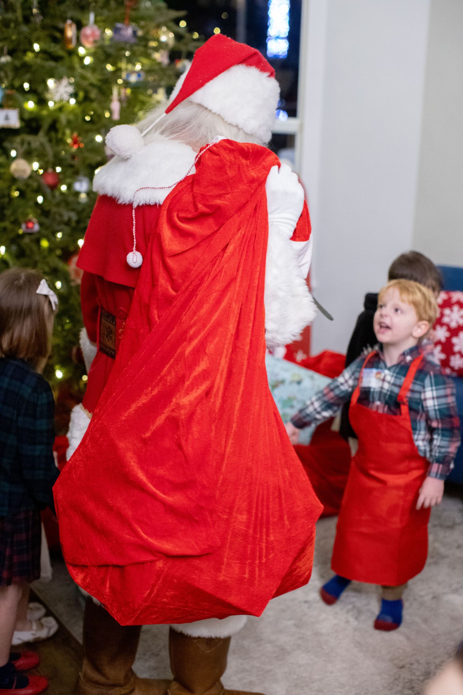 Santa Claus in traditional red suit interacting with children near a Christmas tree.