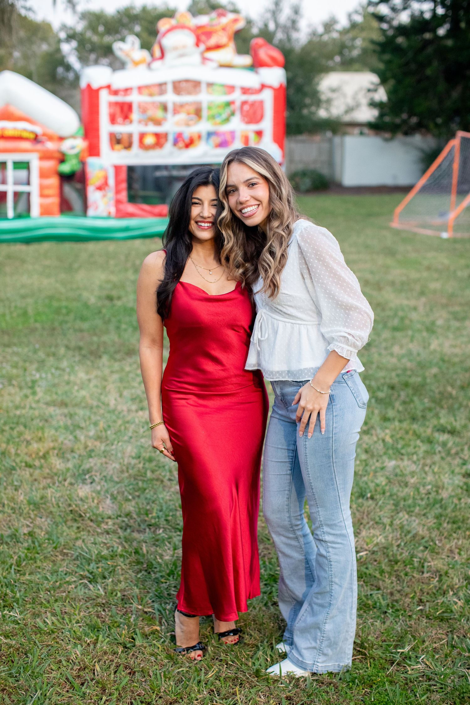 Two people pose casually on grass with carnival attractions and bouncy houses in background.