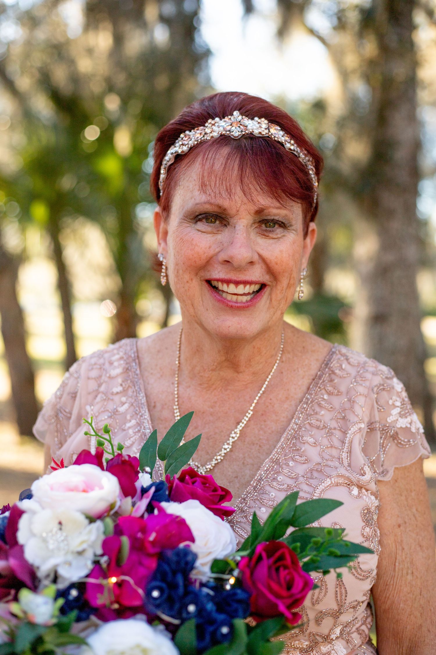 Bride wearing pink lace dress and tiara holds vibrant bouquet with roses and orchids.