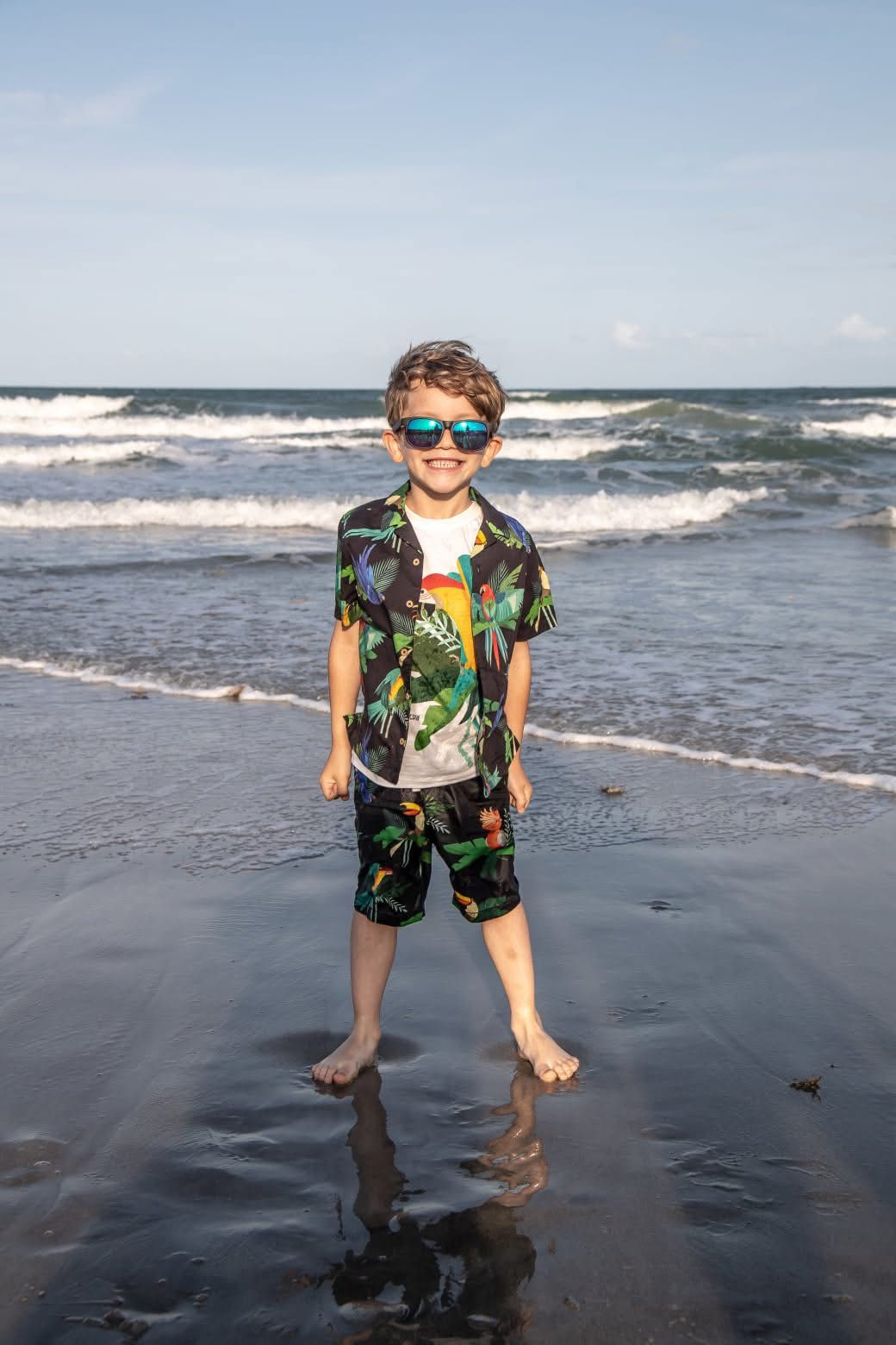 Playing in the ocean waves wearing a tropical print shirt and blue sunglasses.