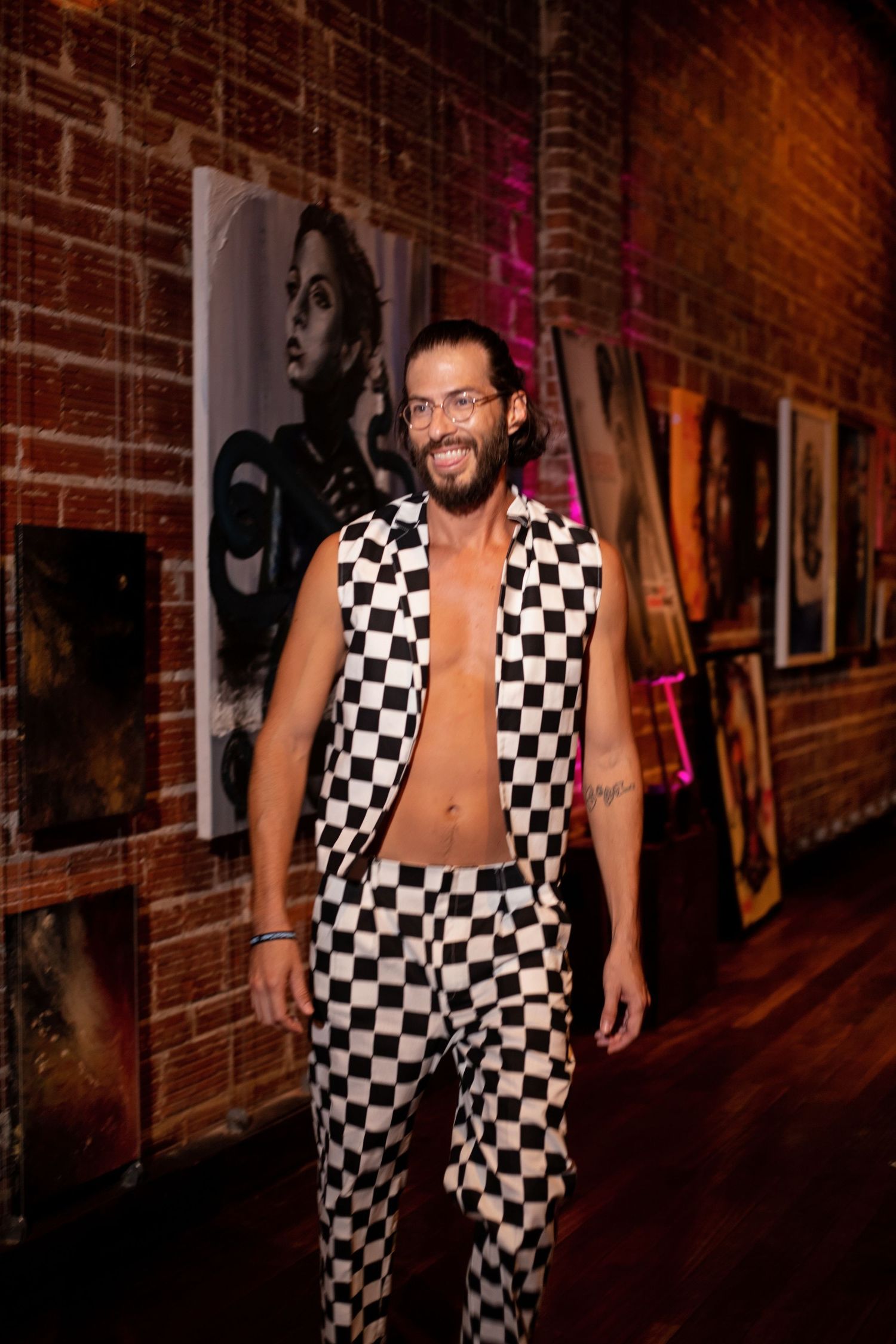 A model wearing a black and white checkered suit poses in front of gallery artwork.