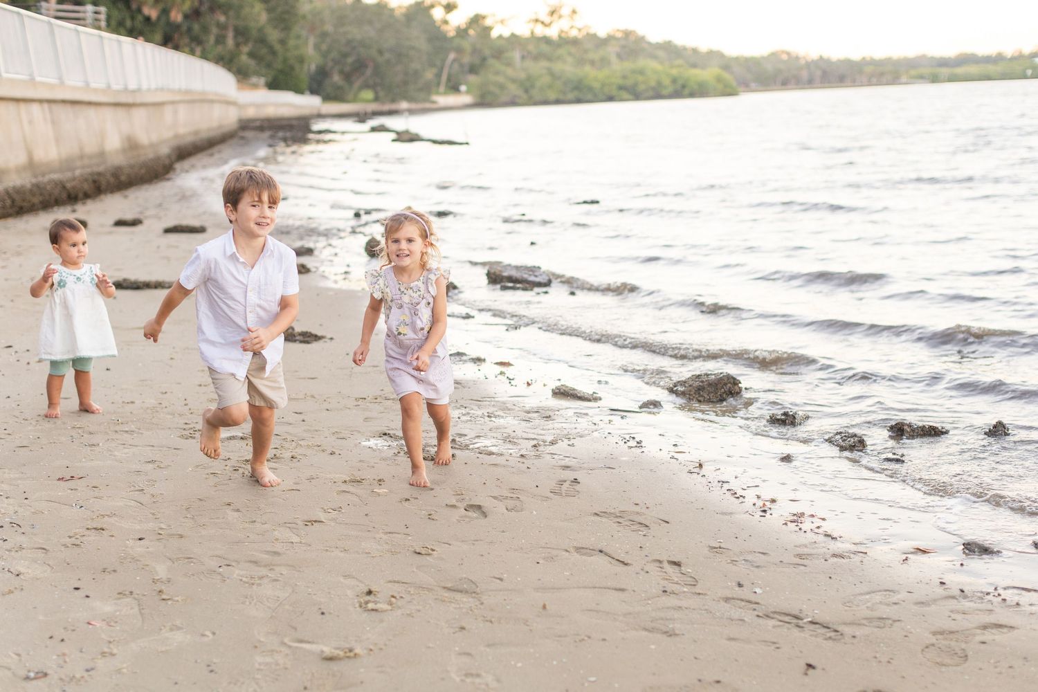 Three happy children running and playing on a sandy beach near the water's edge on a sunny day.