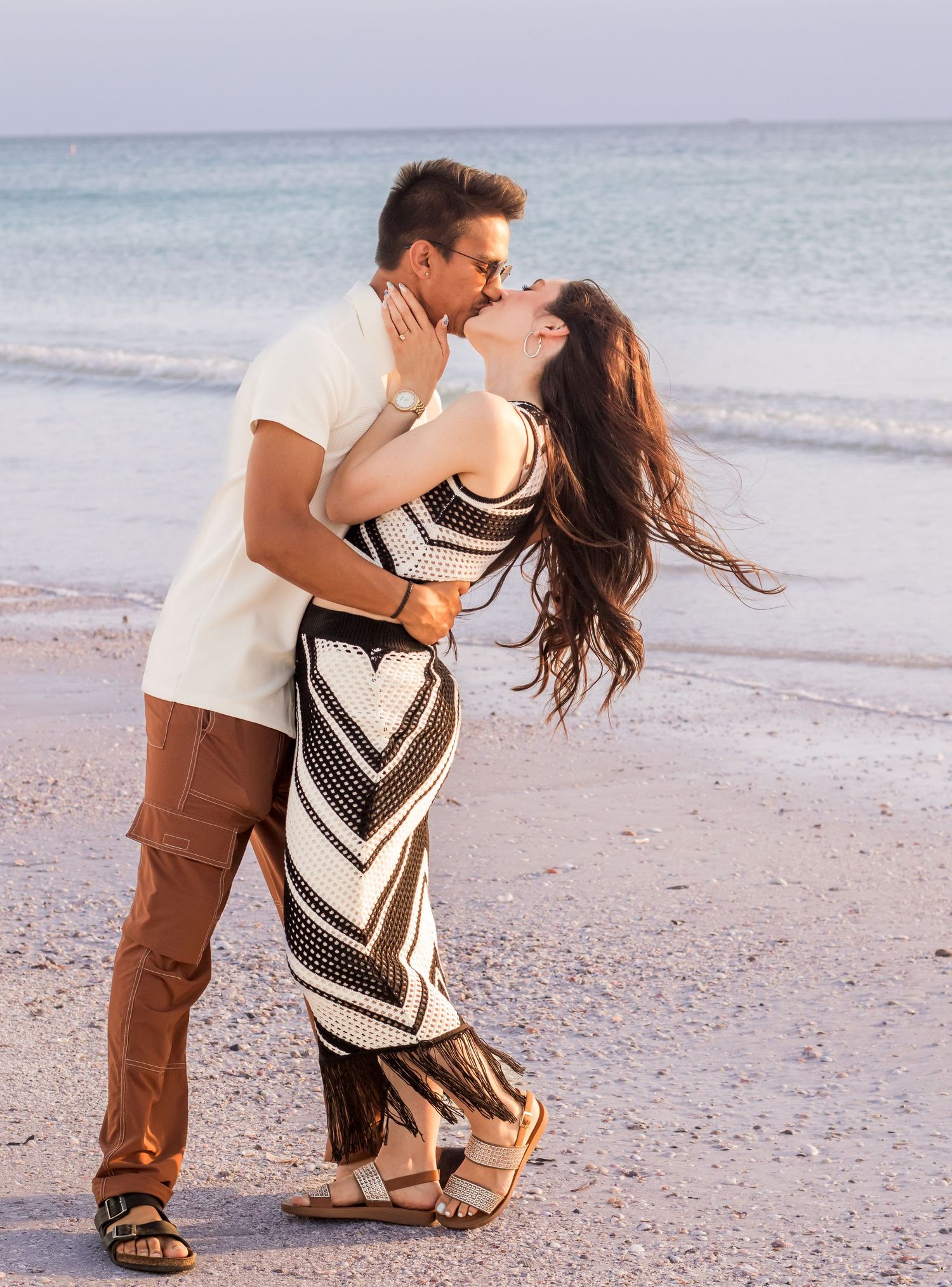 Couple dancing together on sandy beach with ocean waves in background.