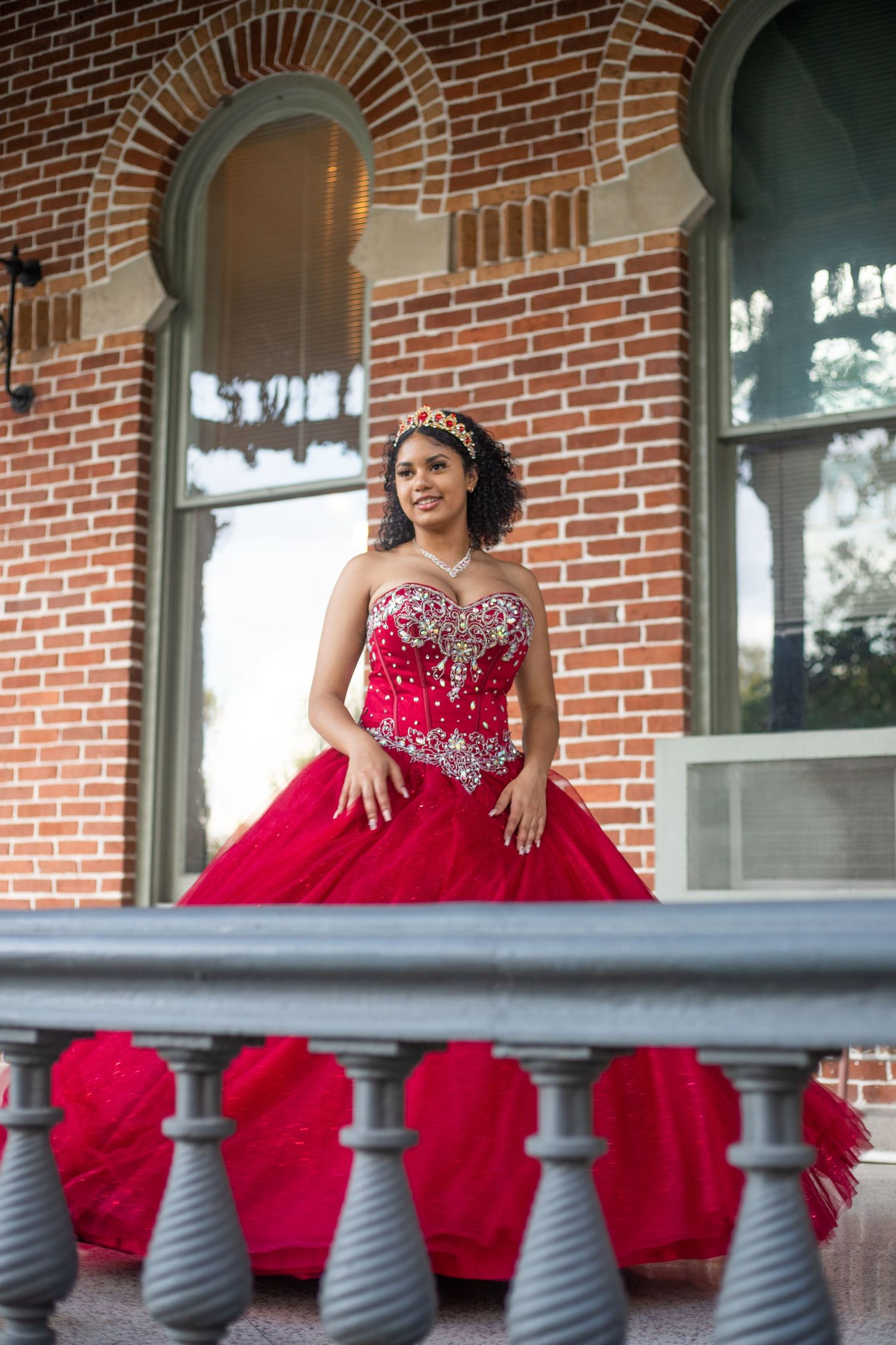 Red formal gown photographed on brick building porch with grey balustrade.
