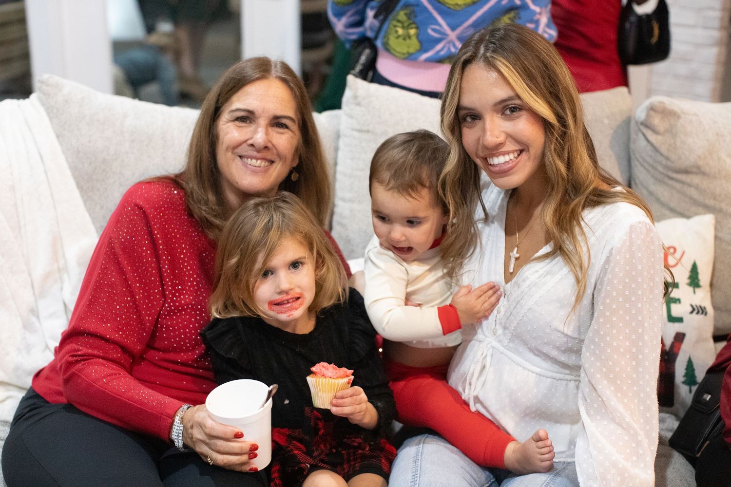 Children gather around Santa Claus during a festive holiday party with Christmas tree in background.
