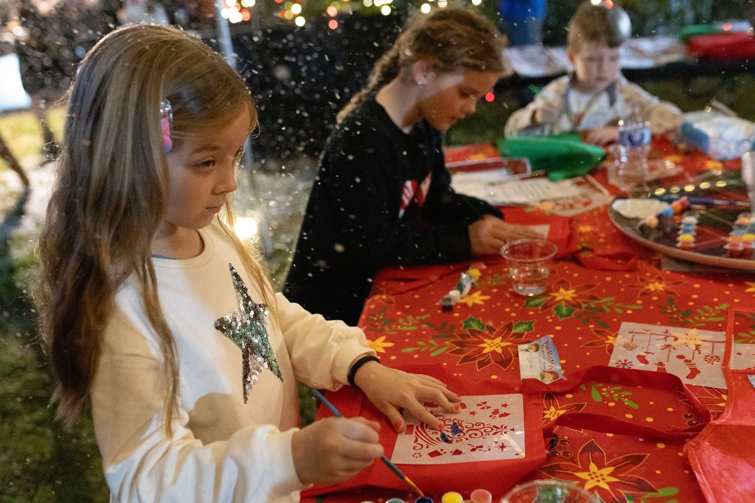 People gathered around tables with red tablecloths participating in holiday activities.