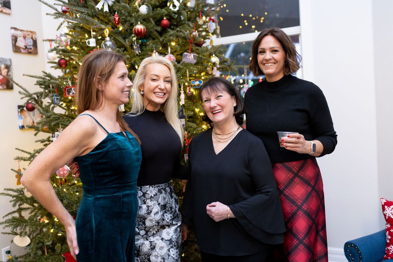 A group stands together smiling in front of a decorated Christmas tree at a holiday gathering.