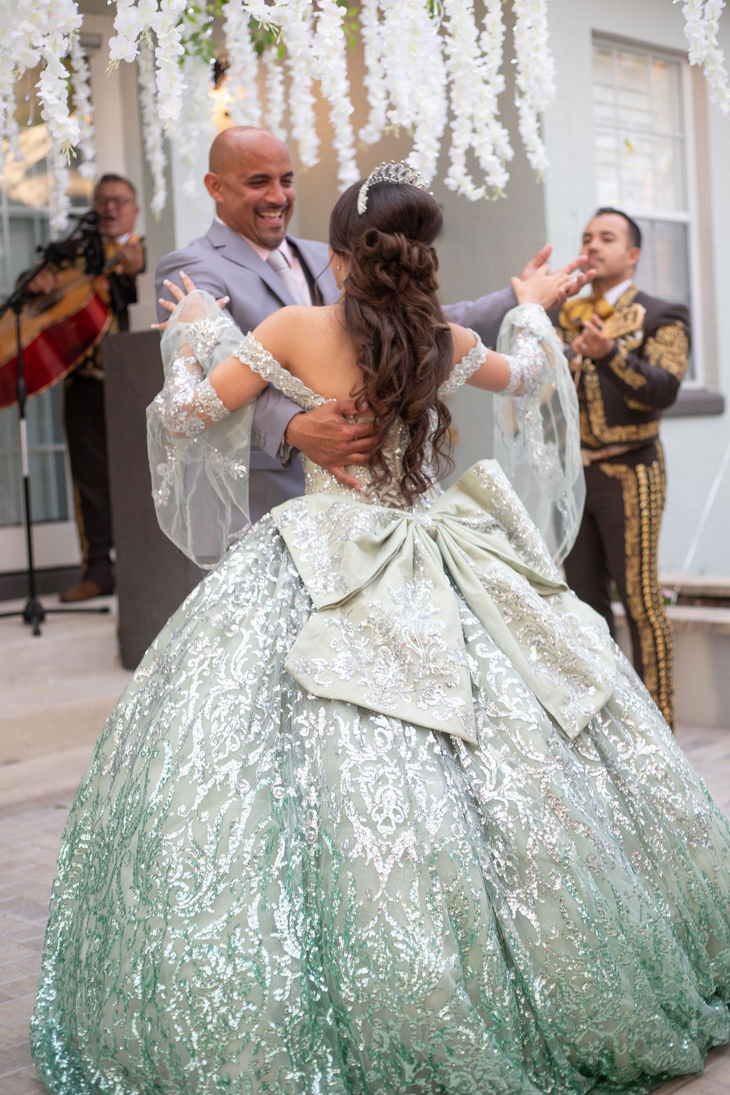 Couple dancing under white floral arrangements with flowing mint green sequined gown.