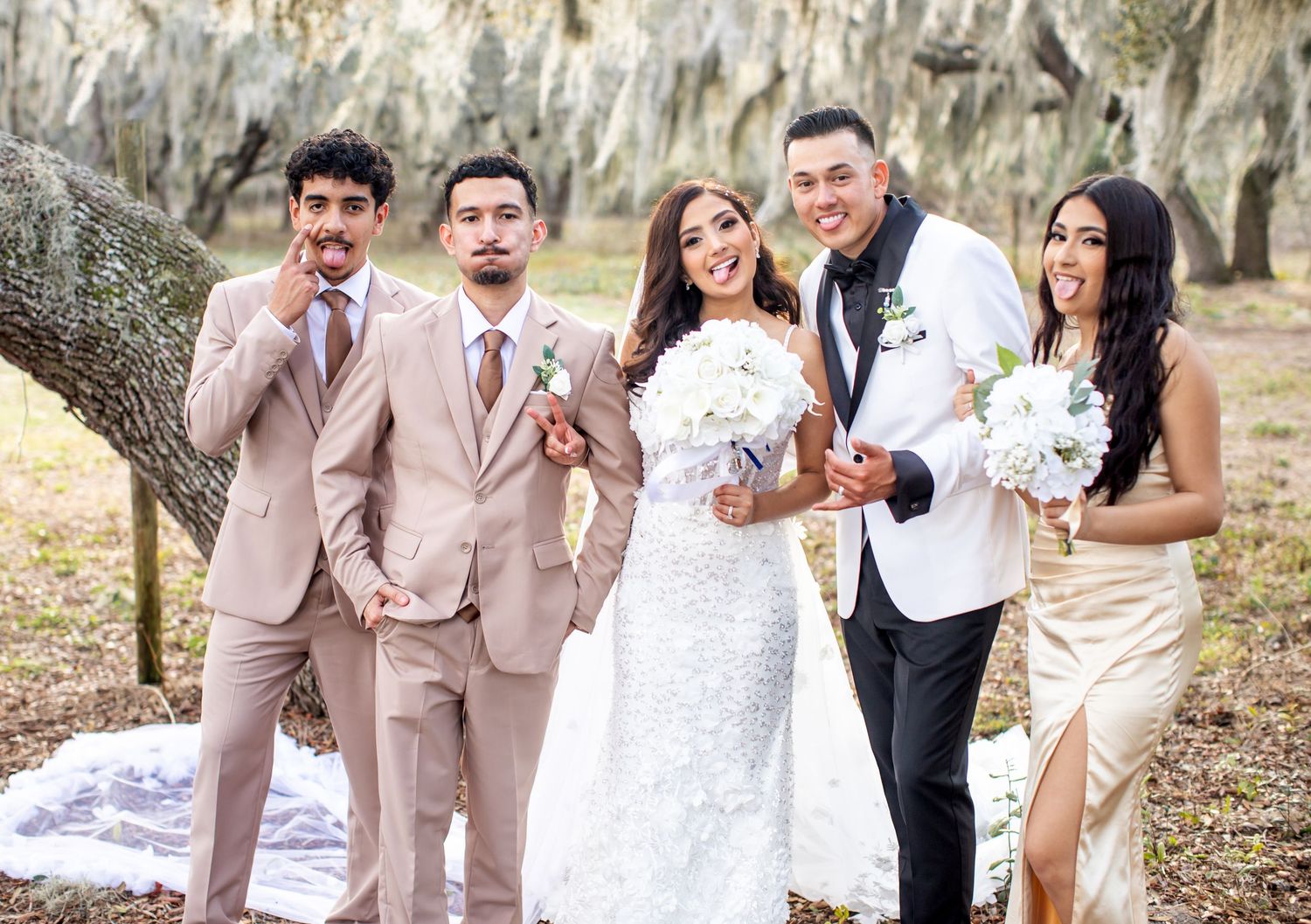 Wedding party of five poses outdoors under moss-covered oak trees, bride in lace gown holding white bouquet.