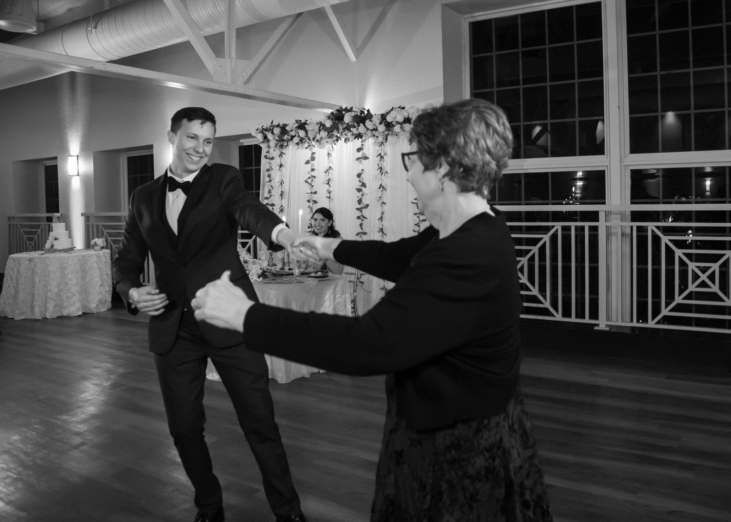 Black and white photo of a groom dancing with an older woman at a wedding reception.
