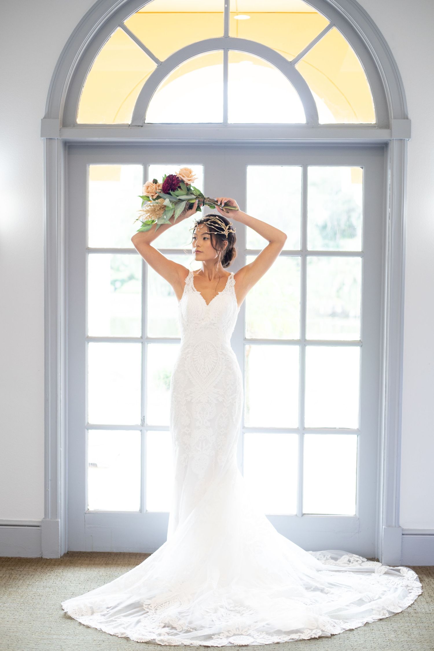 Dramatic bridal portrait in front of arched windows with flowing cathedral veil.