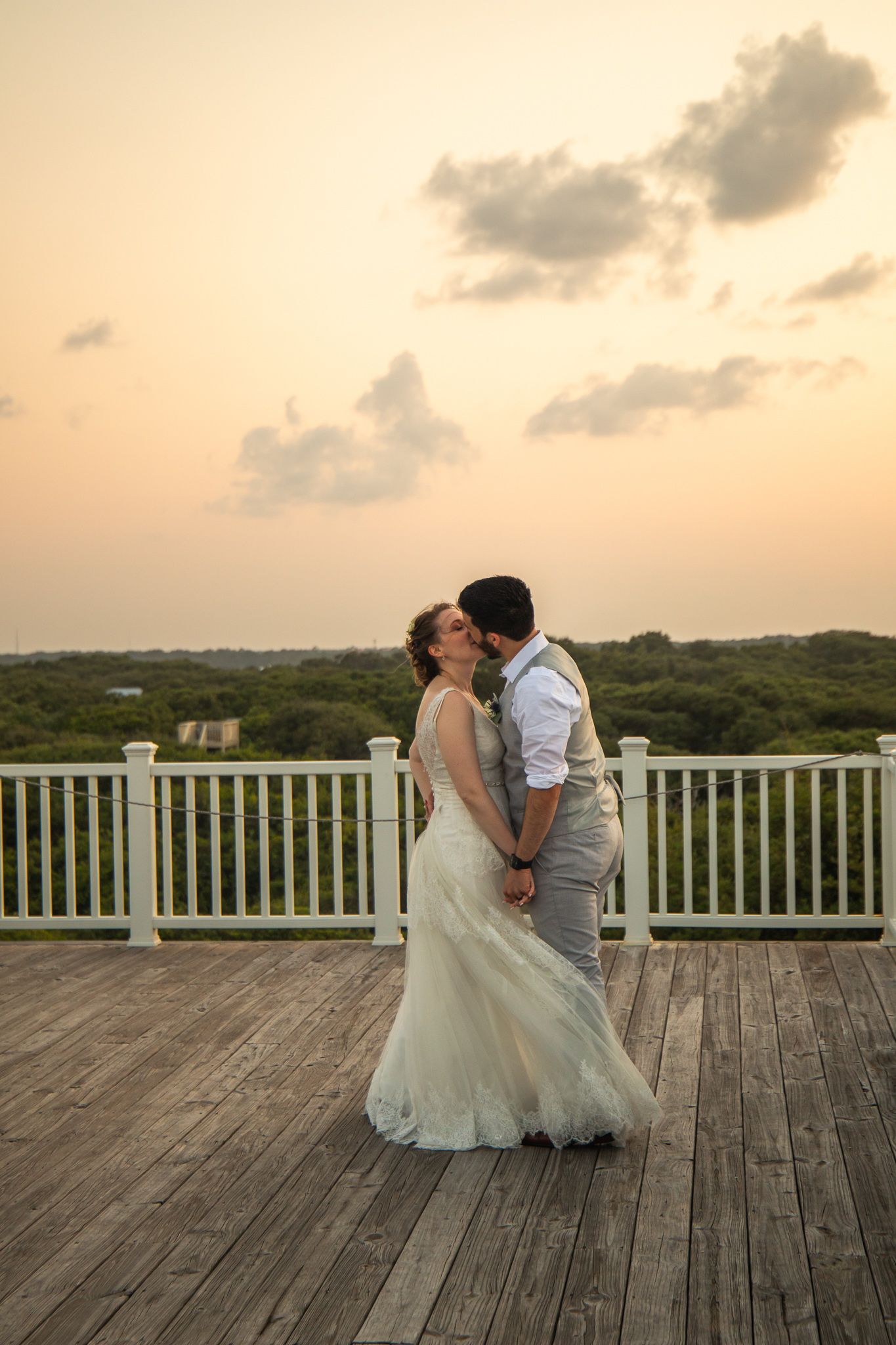 Sunset wedding portraits on wooden deck with dramatic sky and castle backdrop.
