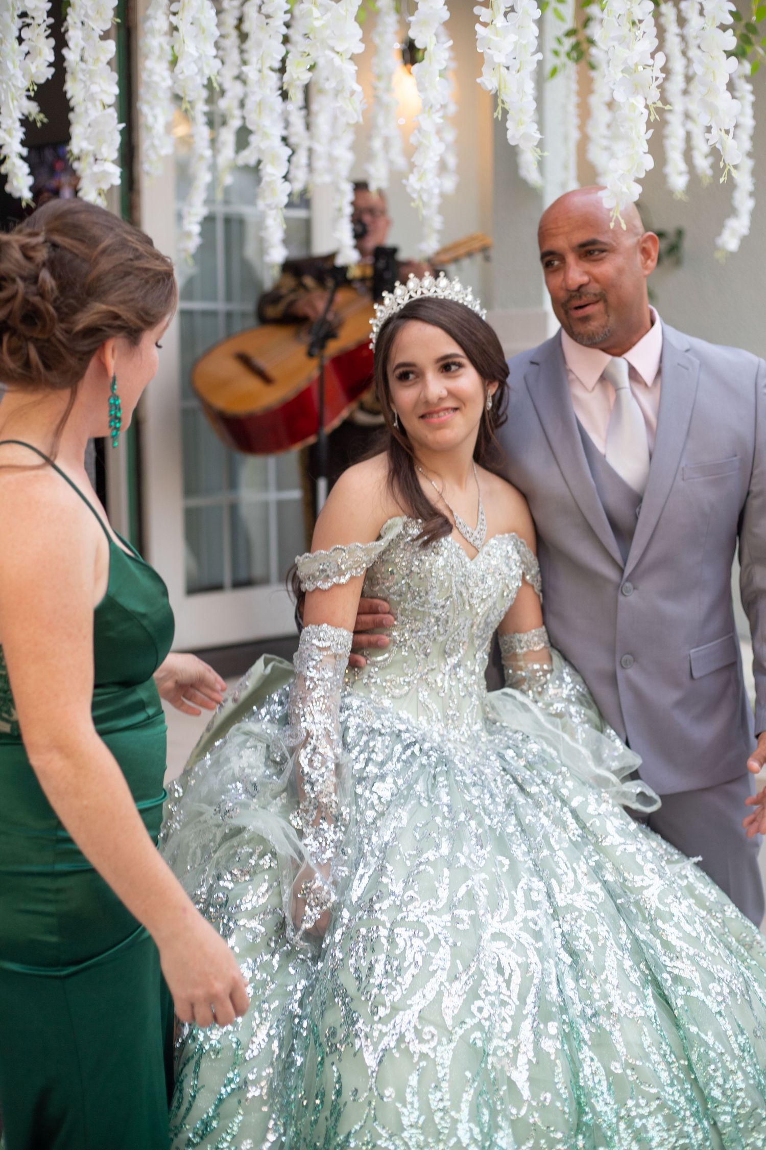 Dancing celebration with mint sequined ballgown and grey suit under hanging white flowers.