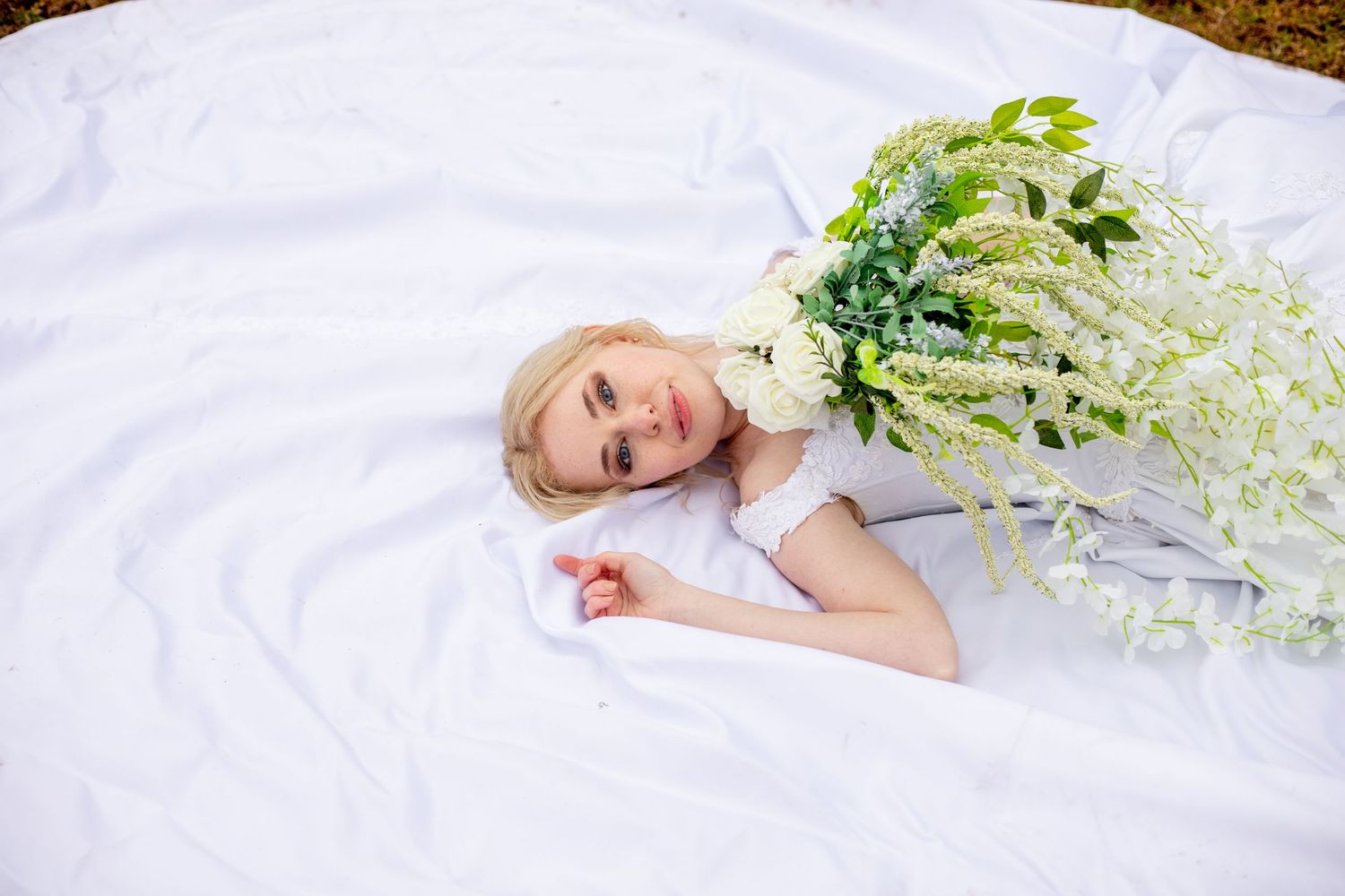 A dreamy portrait of someone lying on white fabric with delicate white flowers.