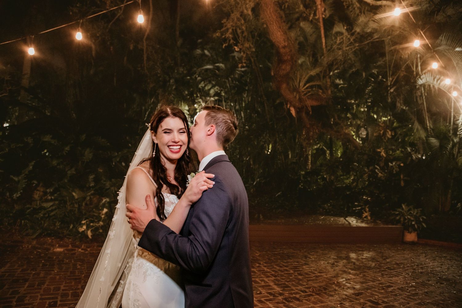 Candid evening wedding portraits with string lights creating a warm romantic atmosphere.