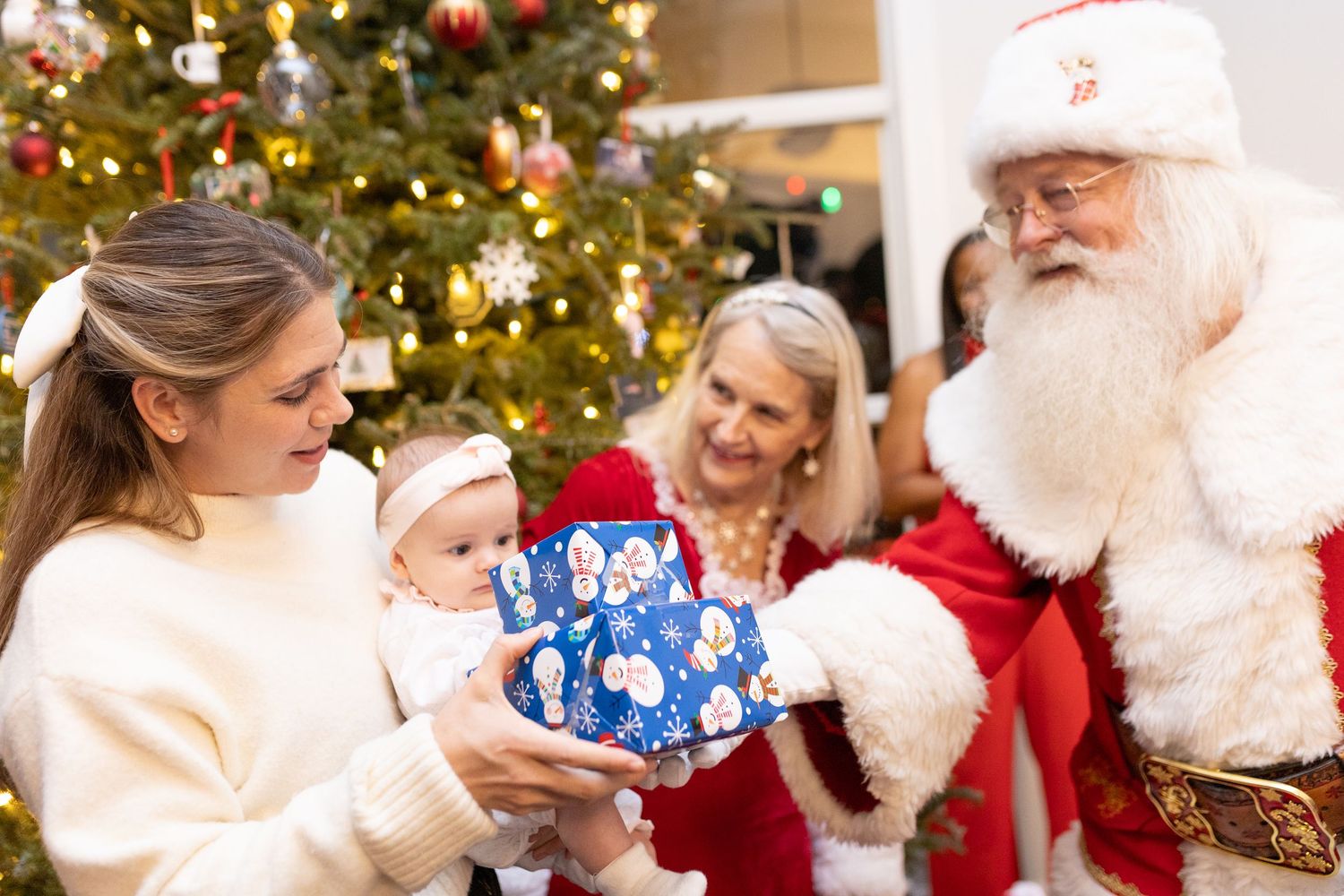 Children in holiday sweaters gather around a decorated Christmas tree with twinkling lights.