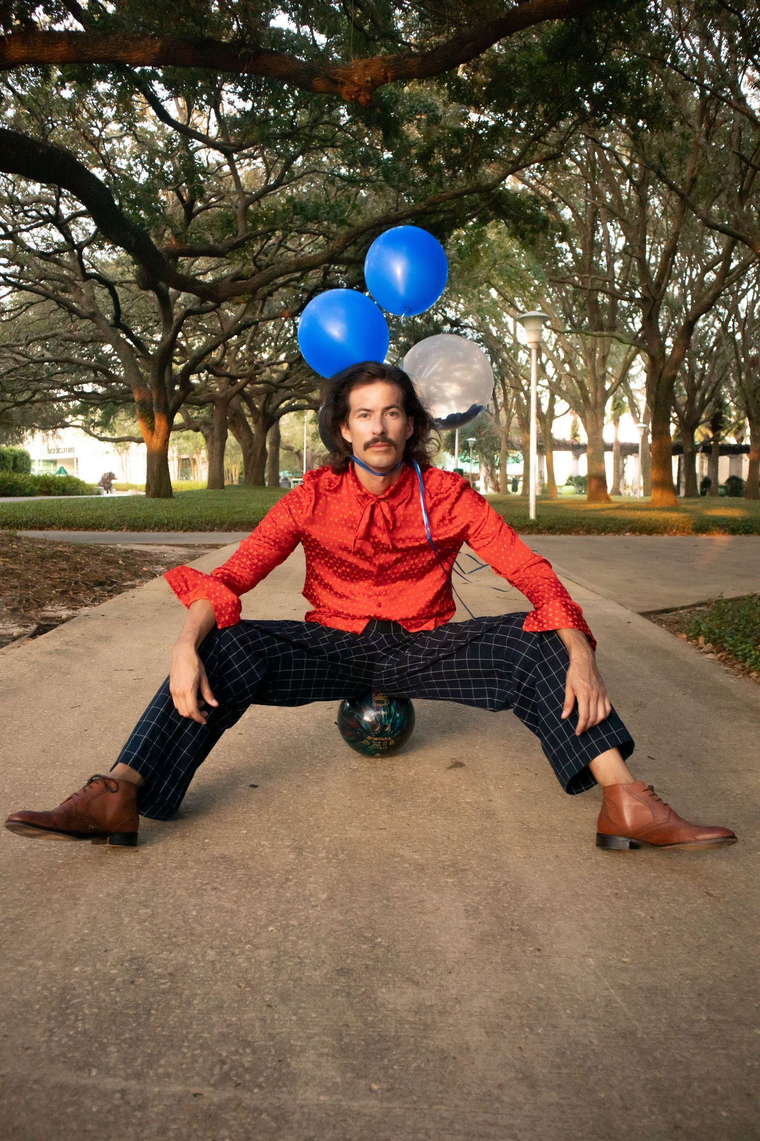 Dramatic pose on pathway with blue balloons and red shirt against tree backdrop.