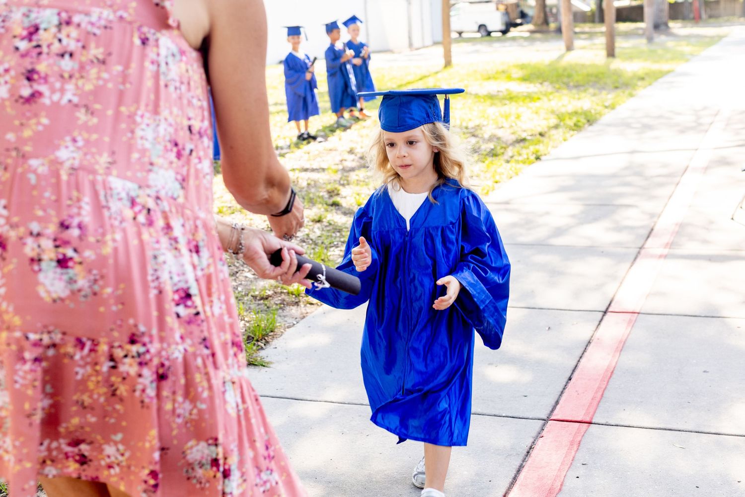 Graduates in blue and pink attire celebrating their achievement outdoors.