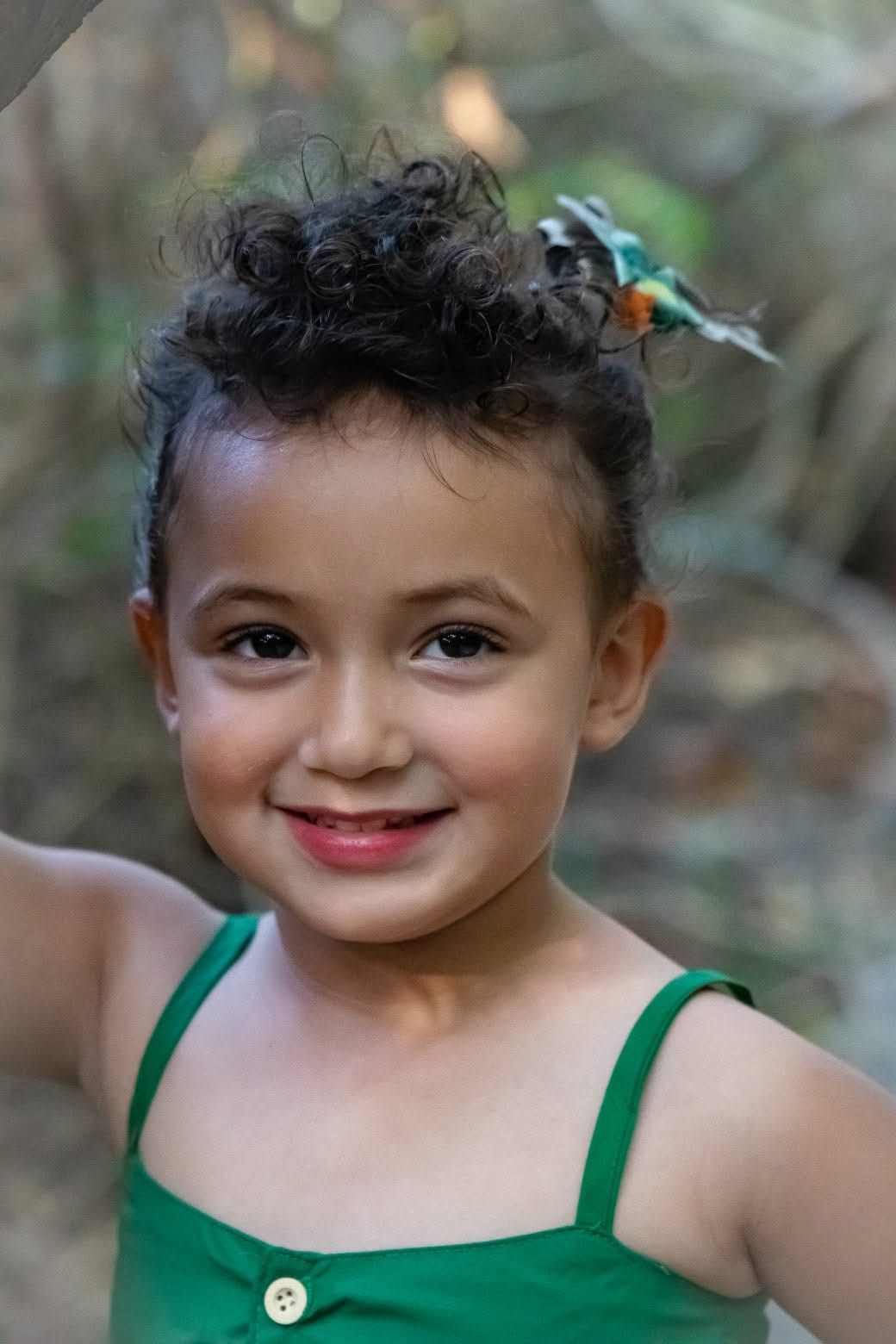 Portrait of a young person in a green tank top with curly hair and a bright smile.
