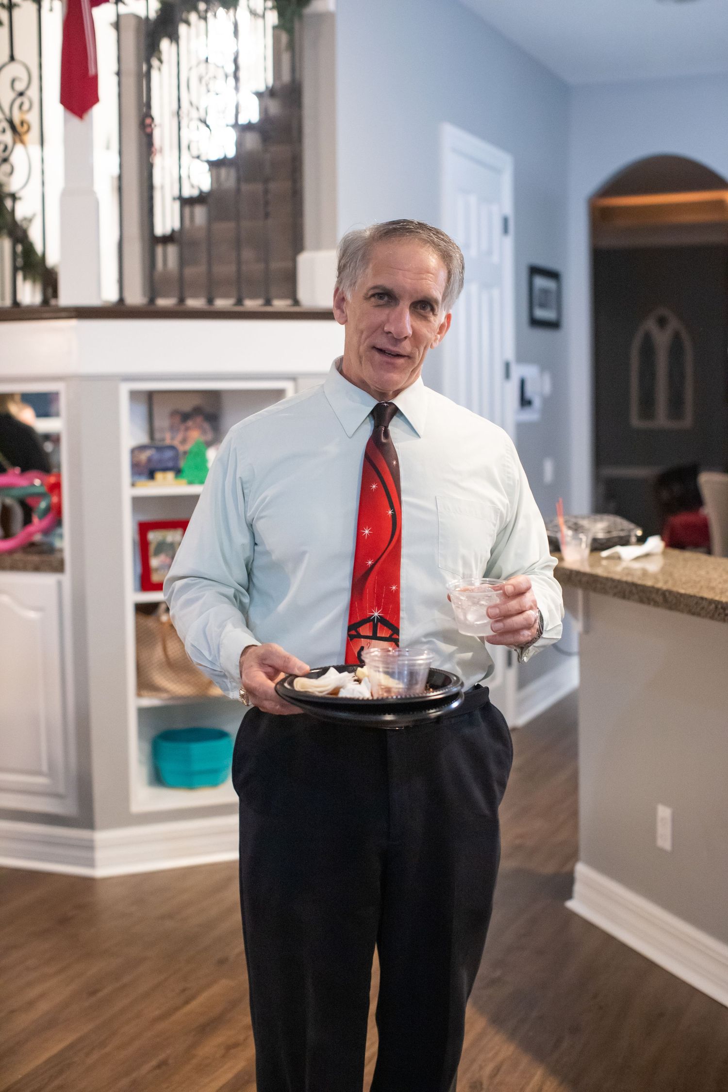 A person in business attire with a red tie holds a serving tray in an elegant home interior.