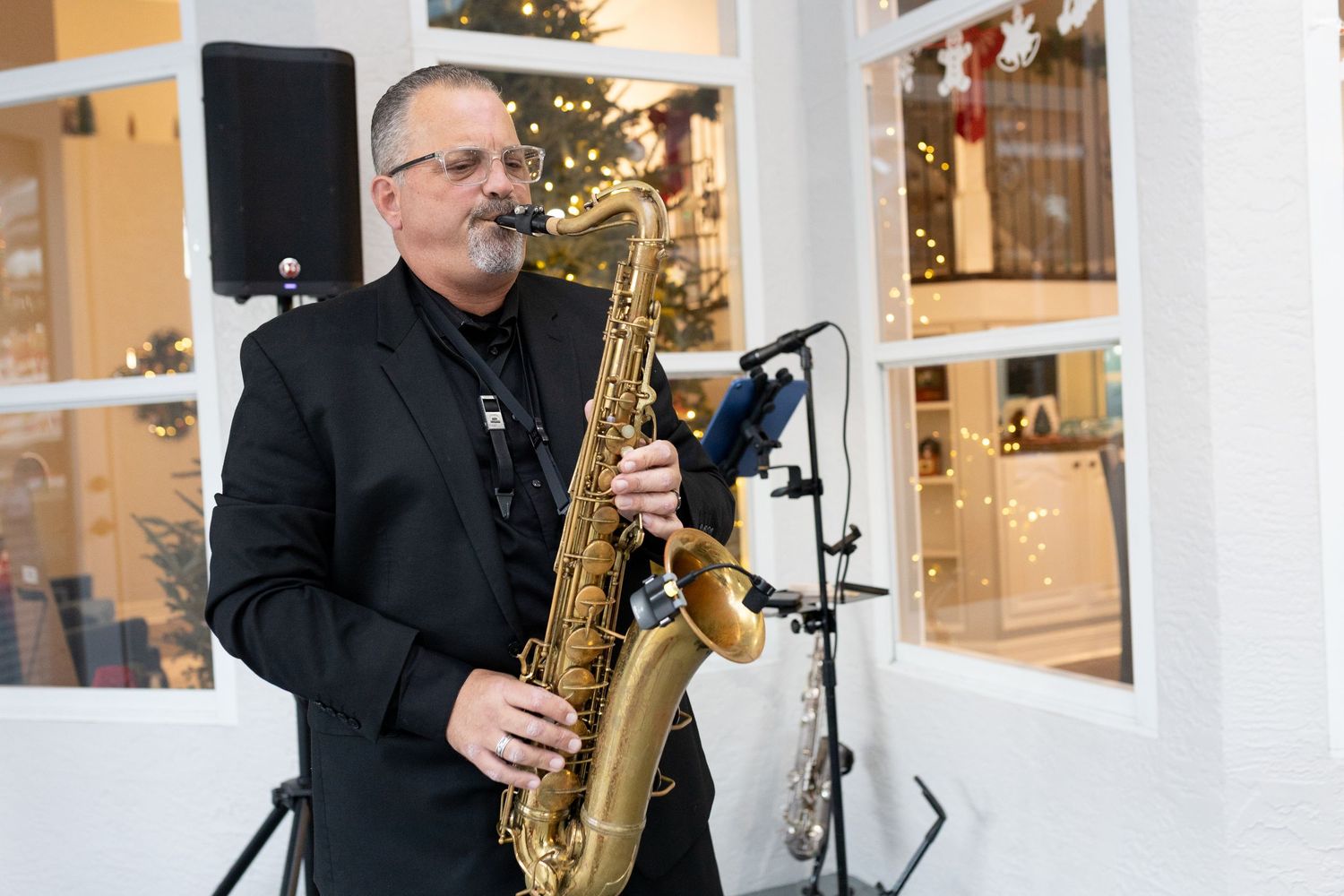 Musician playing saxophone during an outdoor performance near white columns.