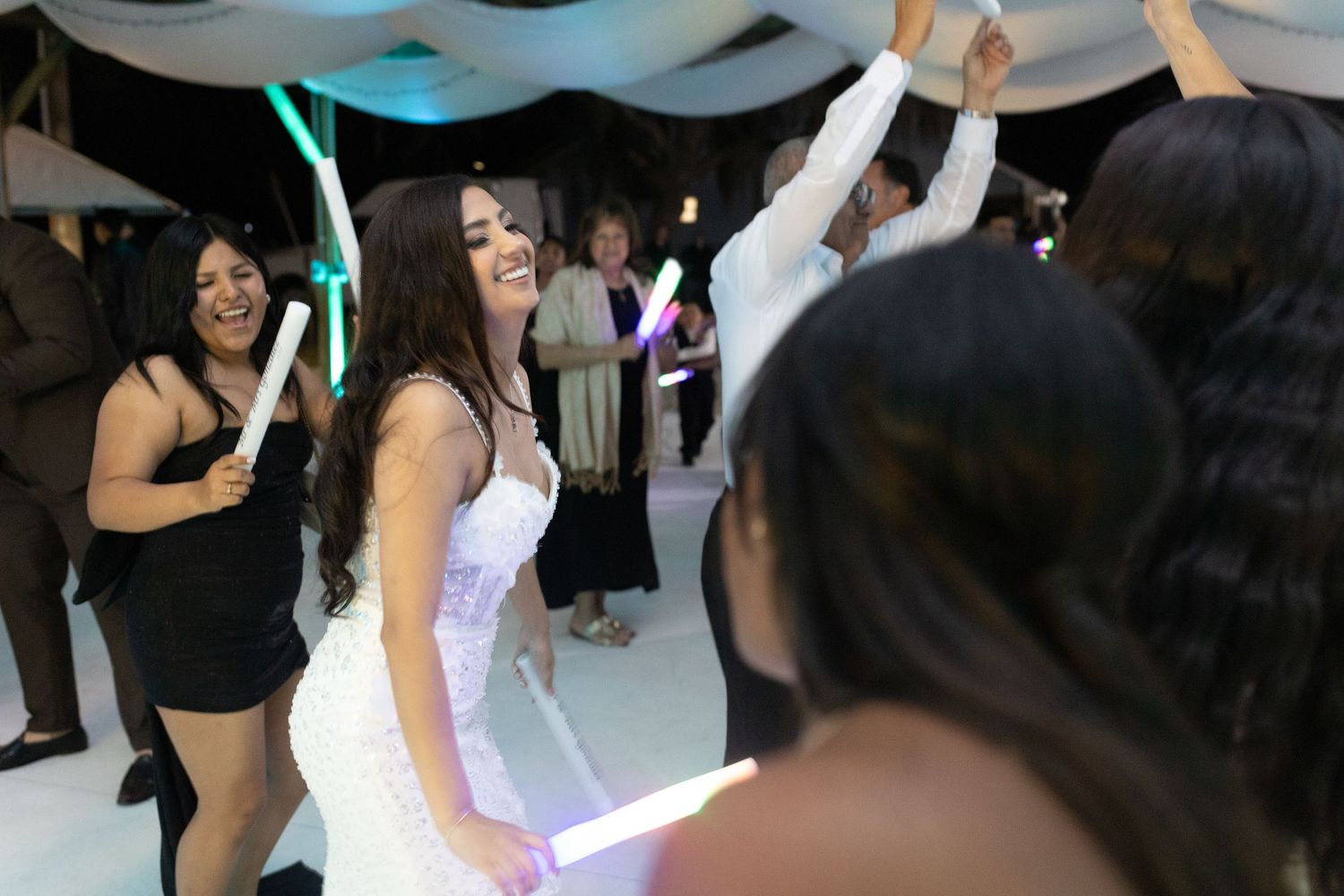 Party guests dancing with colorful LED light wands during an evening wedding reception.
