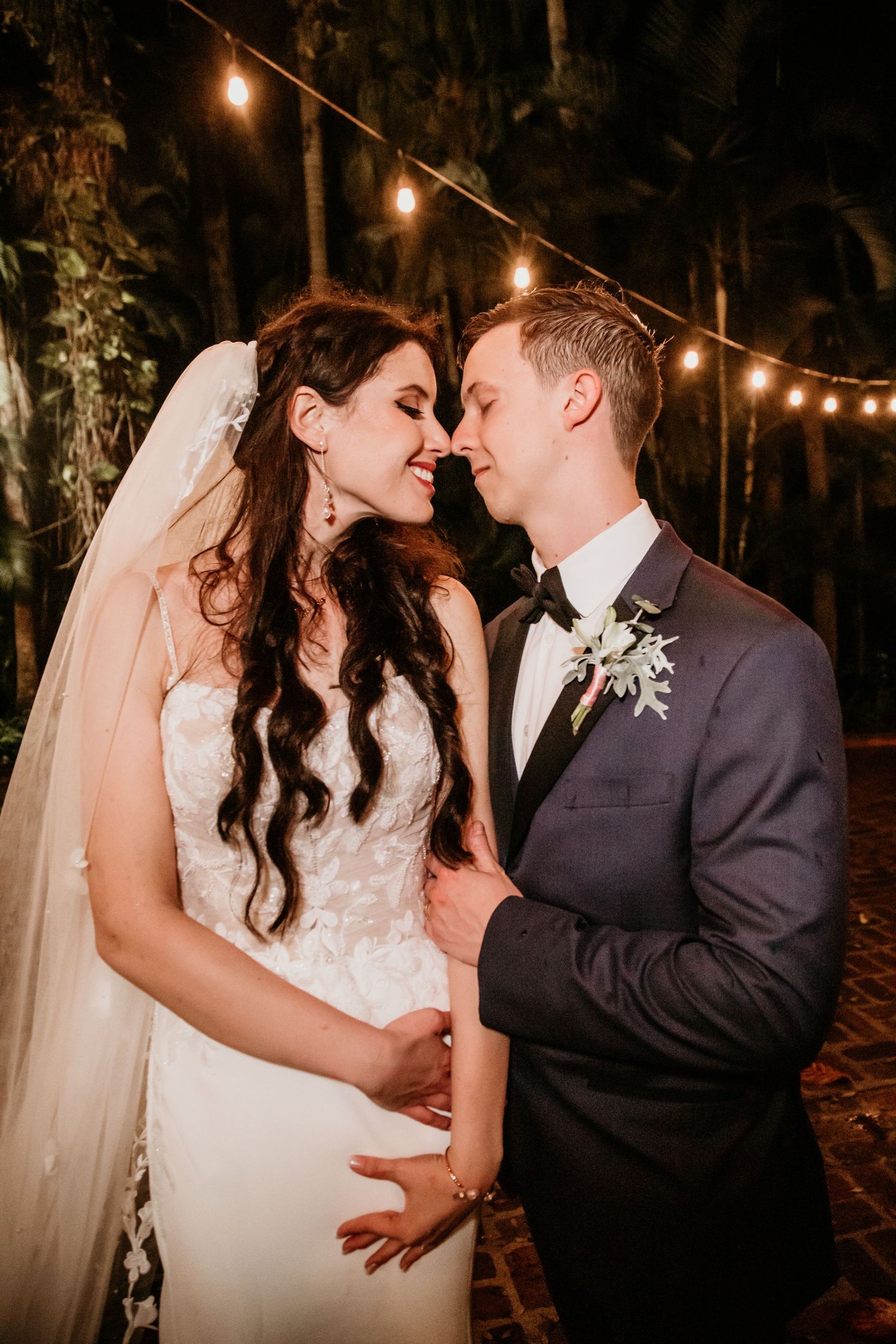 Intimate wedding portraits captured under warm string lights in an outdoor garden setting.