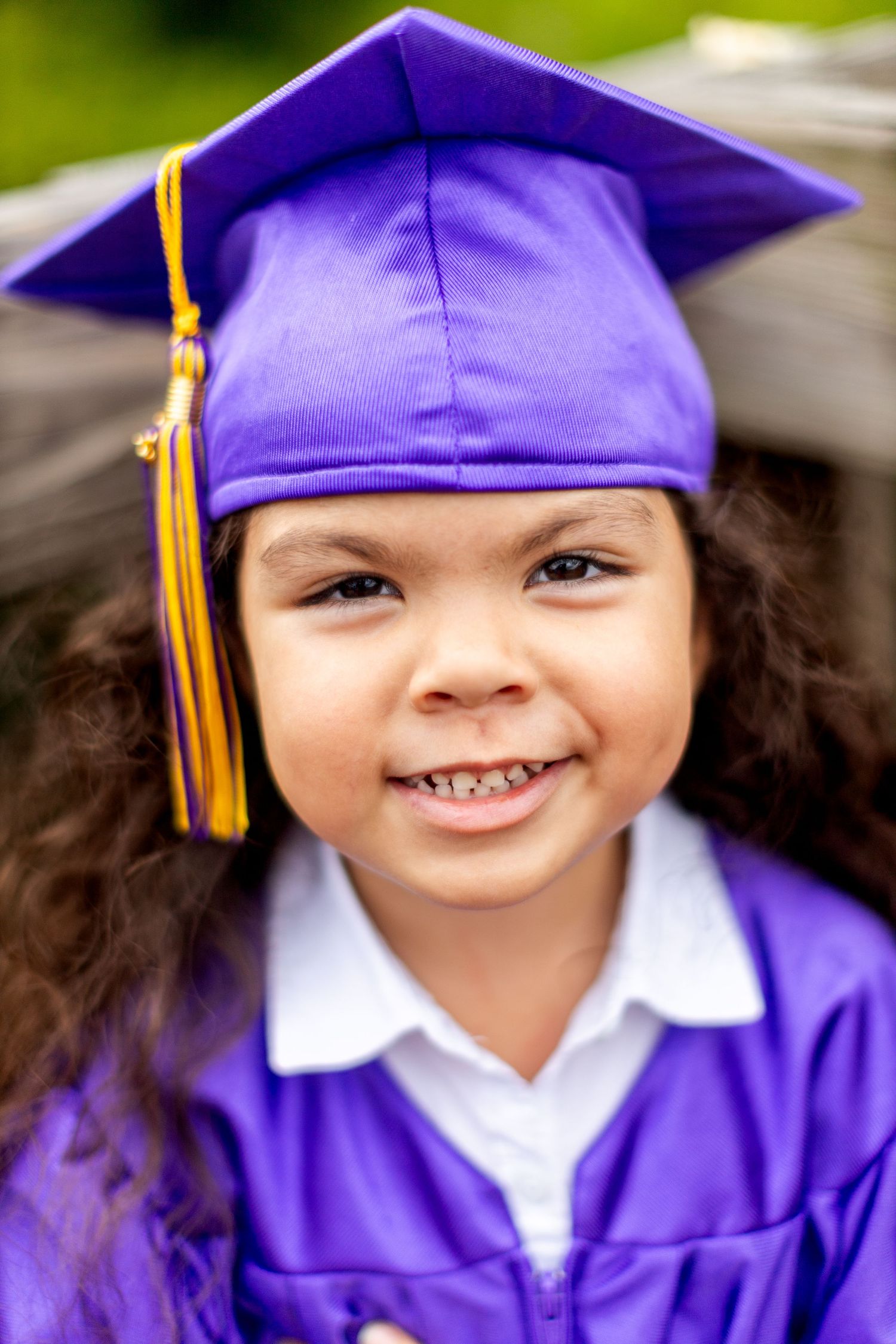 Close up portrait of graduate in purple cap with gold tassel showing joyful expression.