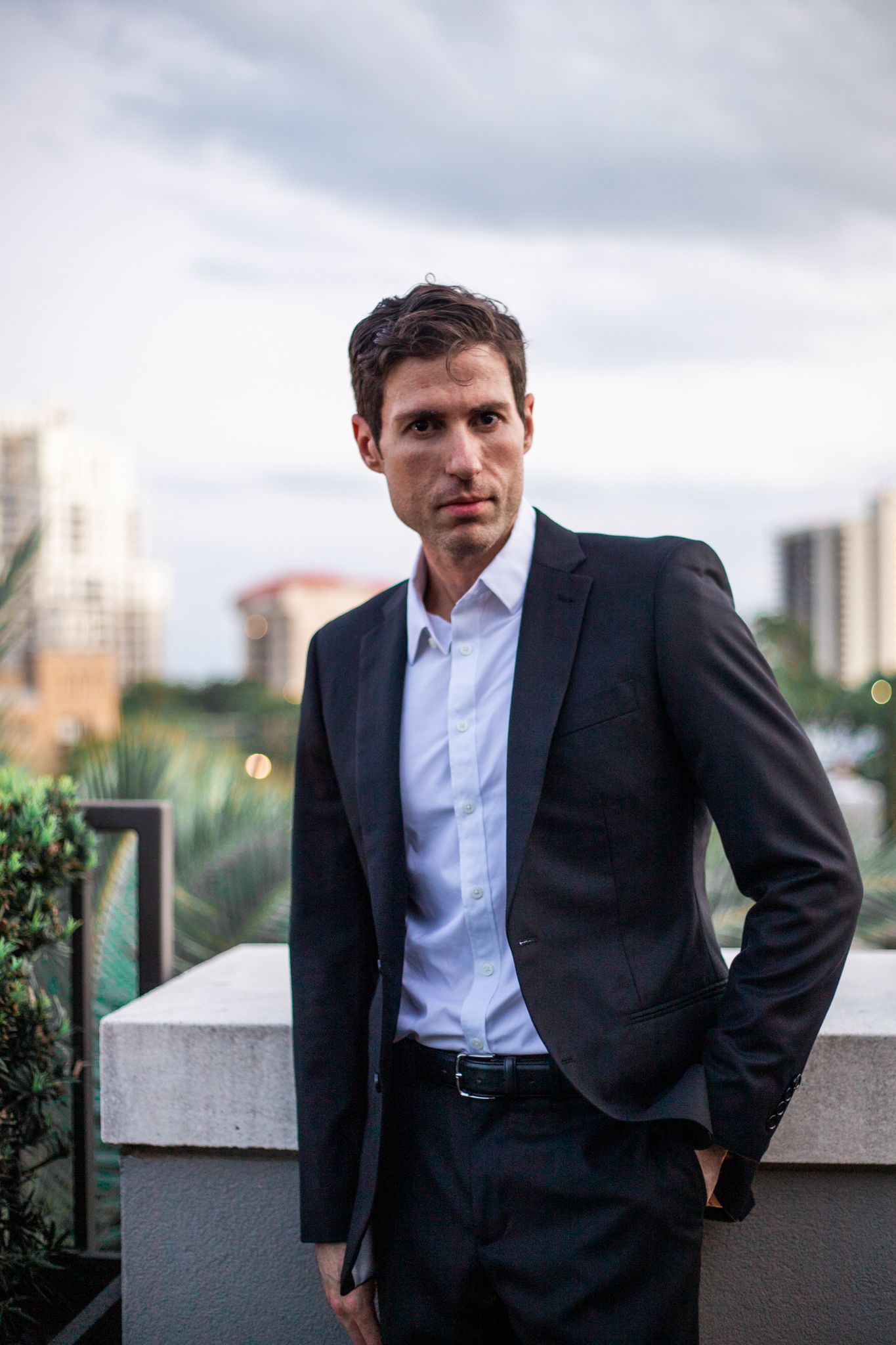 Professional portrait of person in business suit against urban skyline backdrop.