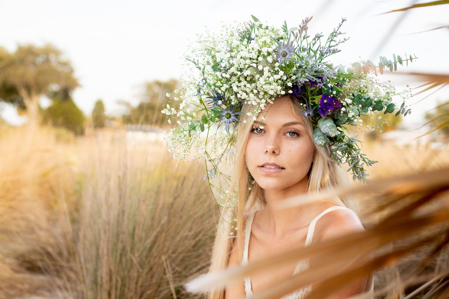 Dreamy close-up portrait with a wildflower and baby's breath crown in a sunlit meadow.