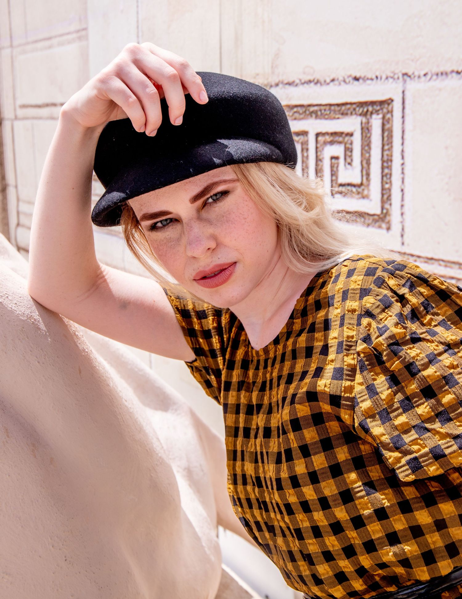 Stylish portrait series showing yellow checkered shirt and black cap against light background.