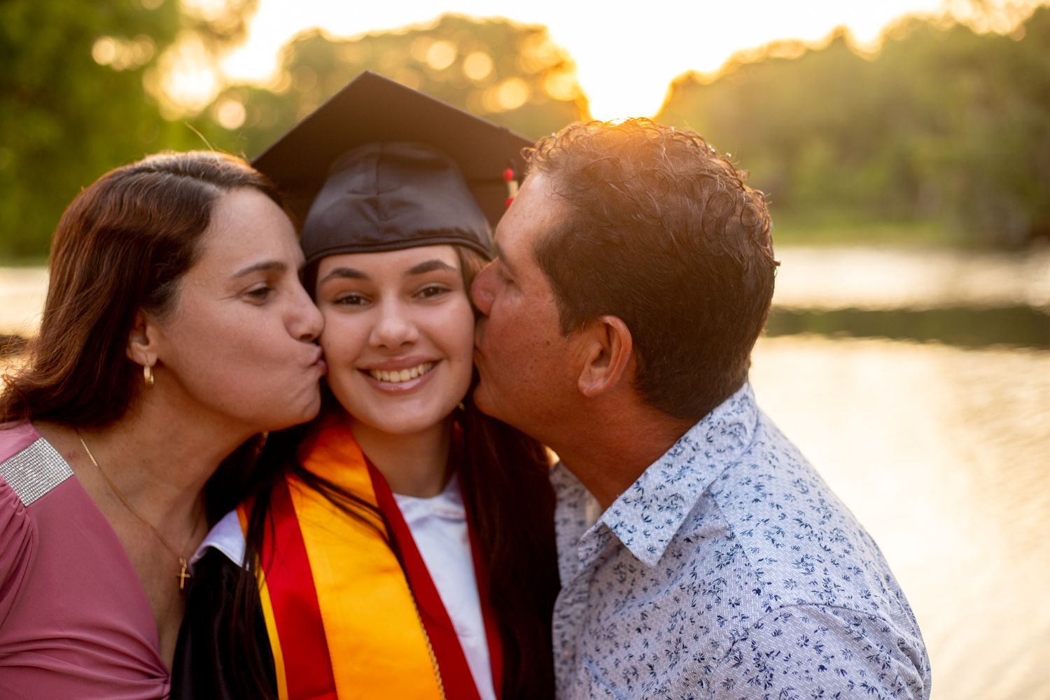 Family members share loving kisses with graduate during sunset celebration.